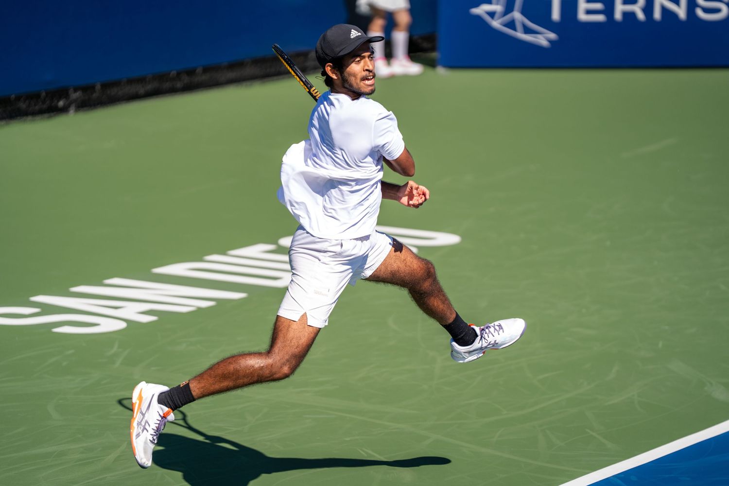 Tennis player sprints to return a shot during a professional outdoor match.