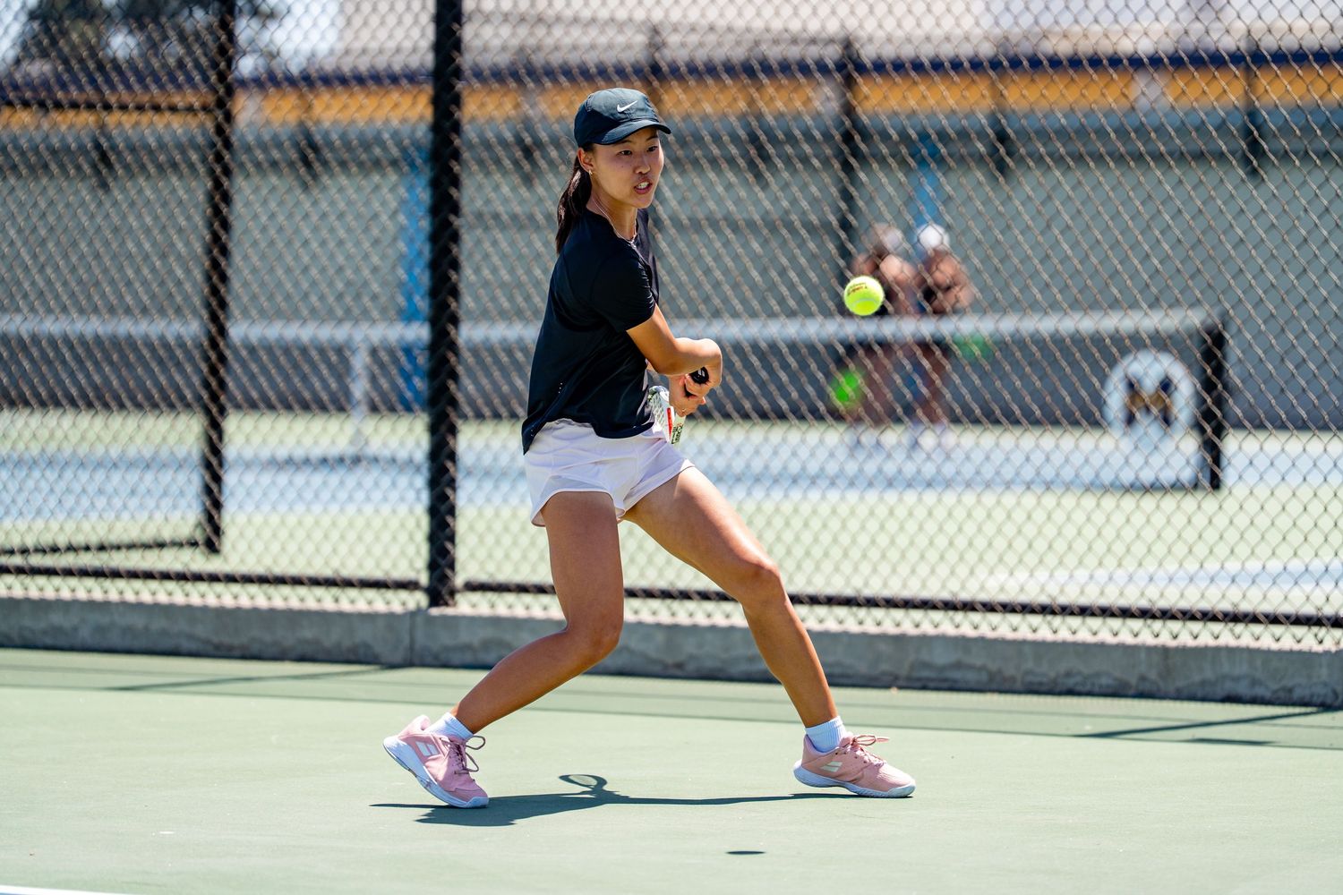 Female tennis player in black top and white skirt hits a forehand on an outdoor court.
