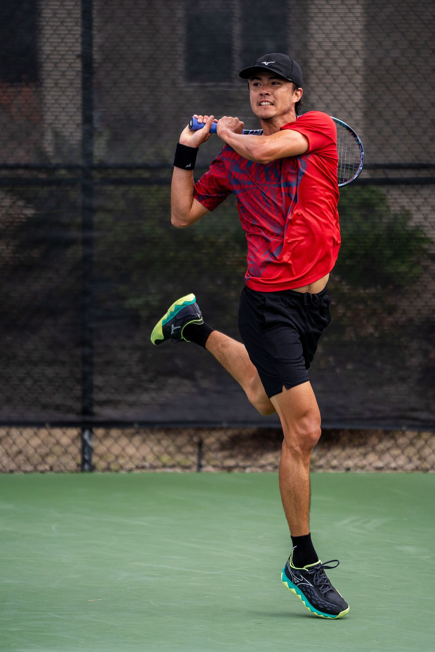 Tennis player in red Nike shirt jumps while hitting overhead shot on court.