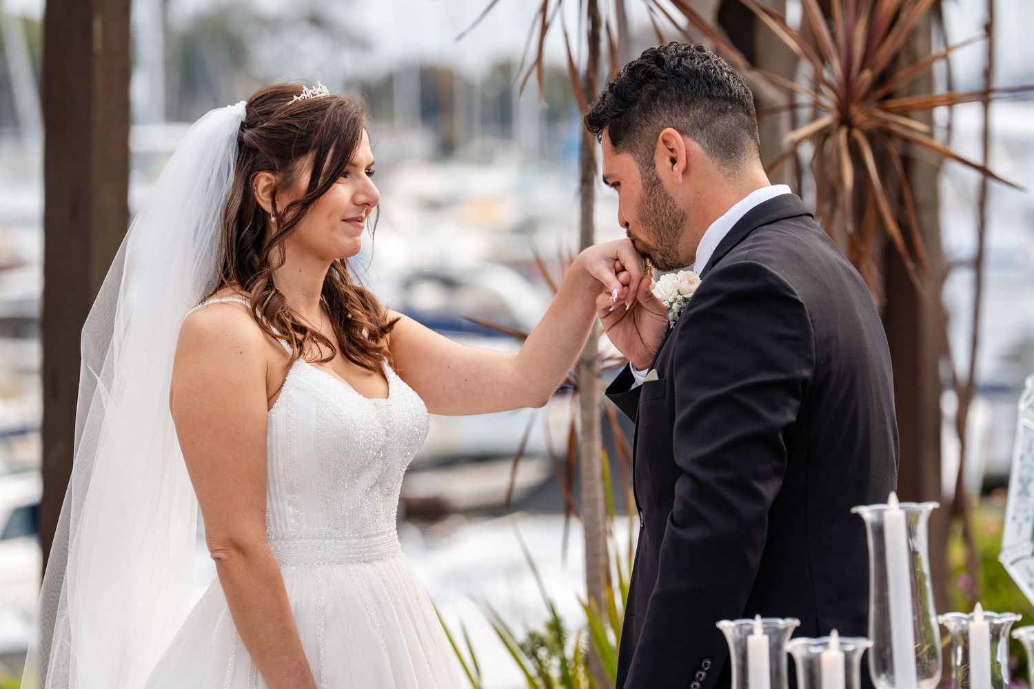 Groom kissing bride's hand during outdoor wedding ceremony at marina.