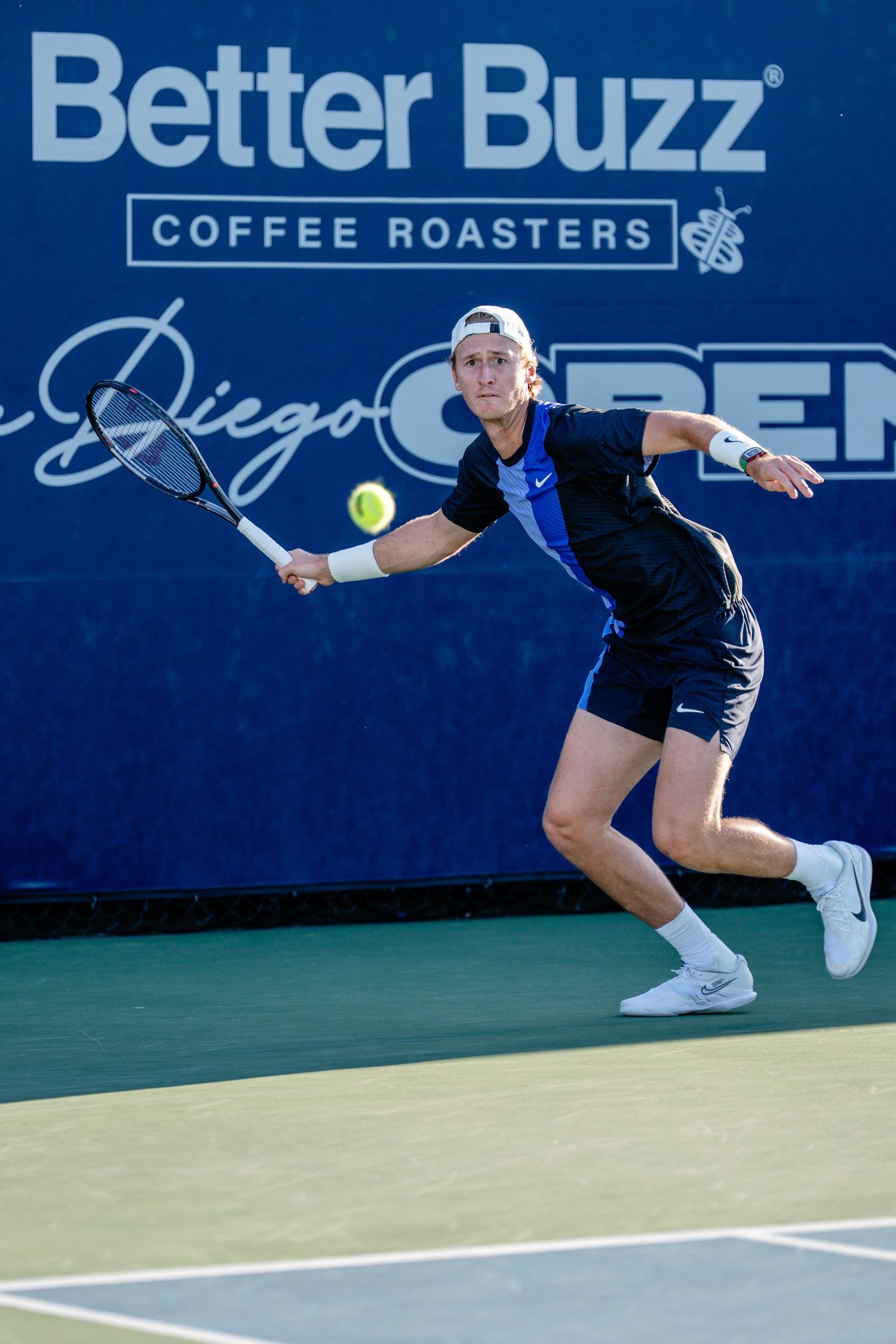 Male tennis player lunges for forehand at Better Buzz Coffee Roasters San Diego Open.