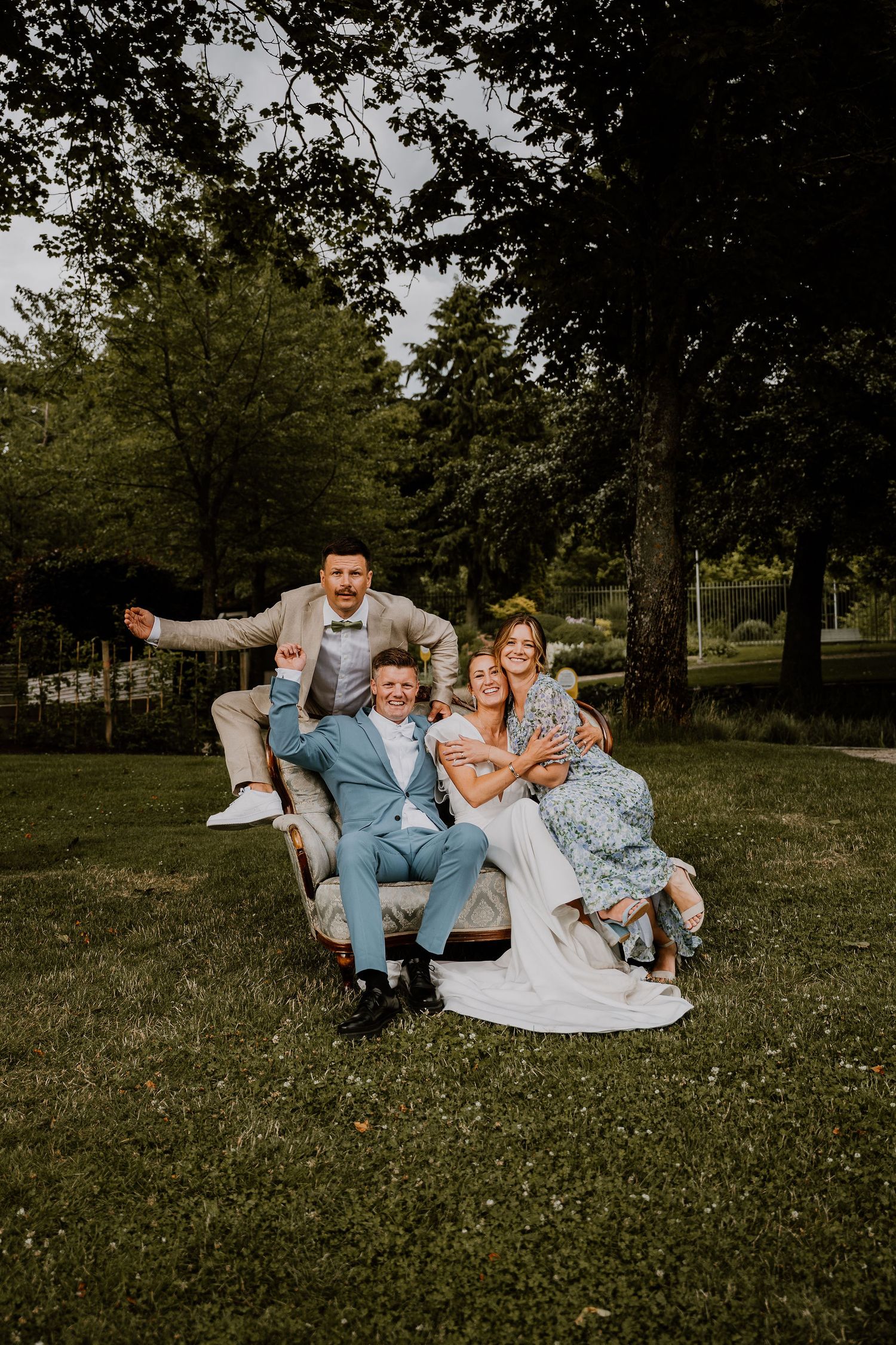 A joyful group sits together on a blanket in the grass, sharing laughter and embraces in a park setting.