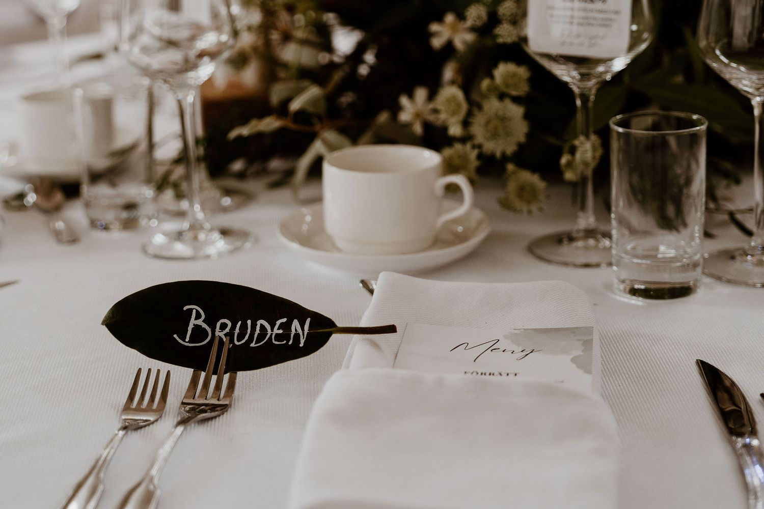Place settings with wine glasses, plates and name cards arranged on an elegant dining table at a formal event.