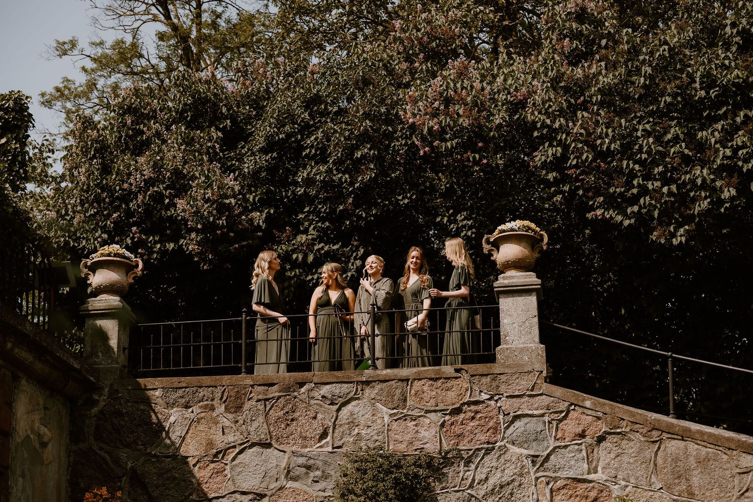 A small group gathers on a rustic stone bridge surrounded by lush green foliage in warm afternoon light.