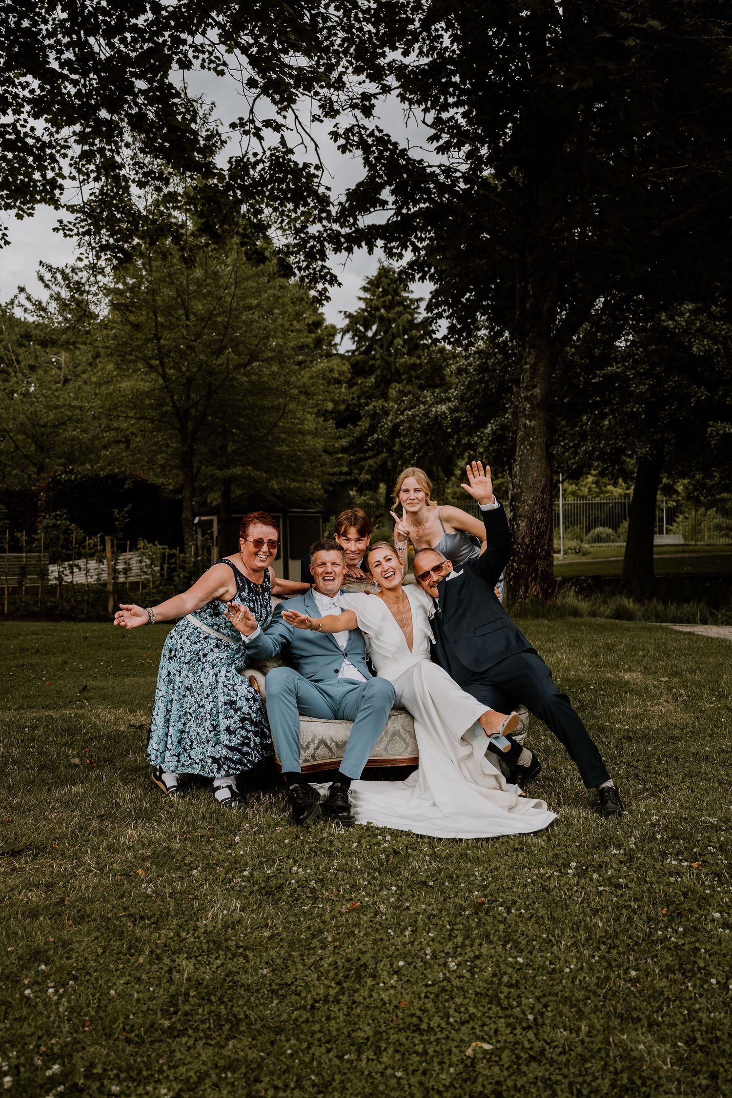 Bridal party lying on grass having fun during outdoor wedding photoshoot in park setting.