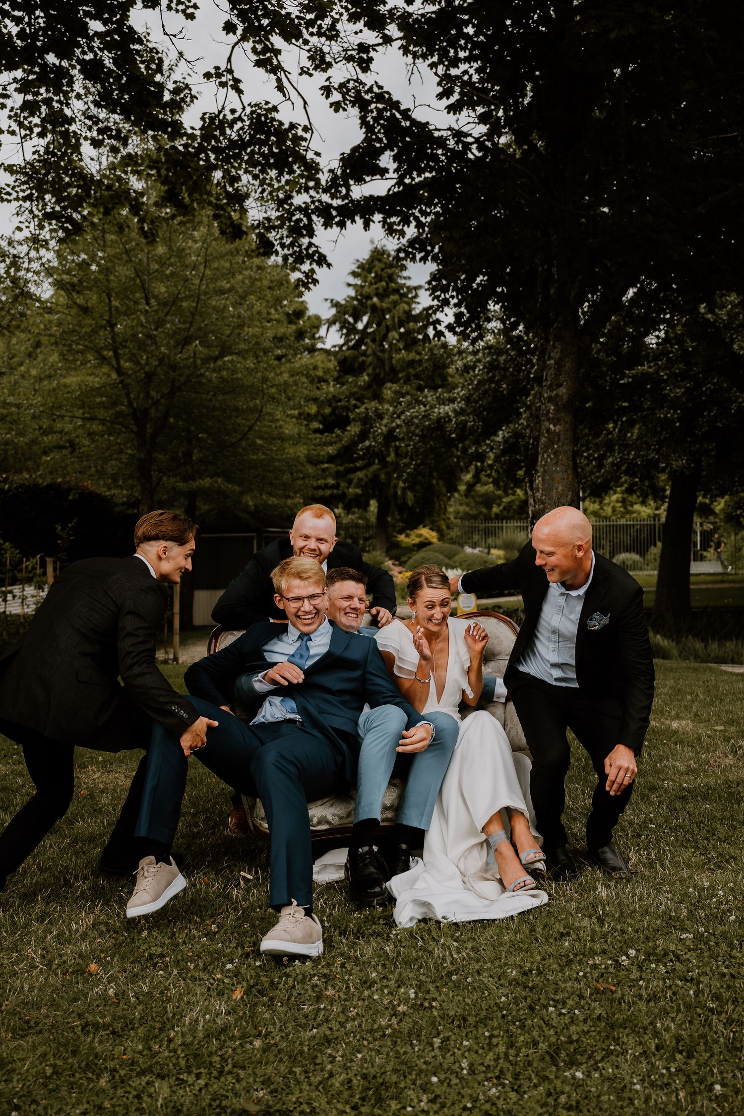 A candid sequence of wedding party members playfully falling onto grassy ground during an outdoor photo session.