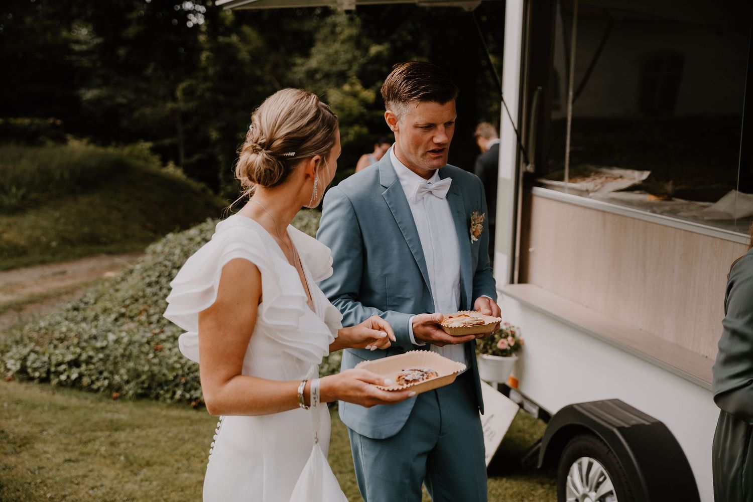 A group of wedding guests enjoy outdoor catering service under a white tent on a sunny day at an elegant reception.