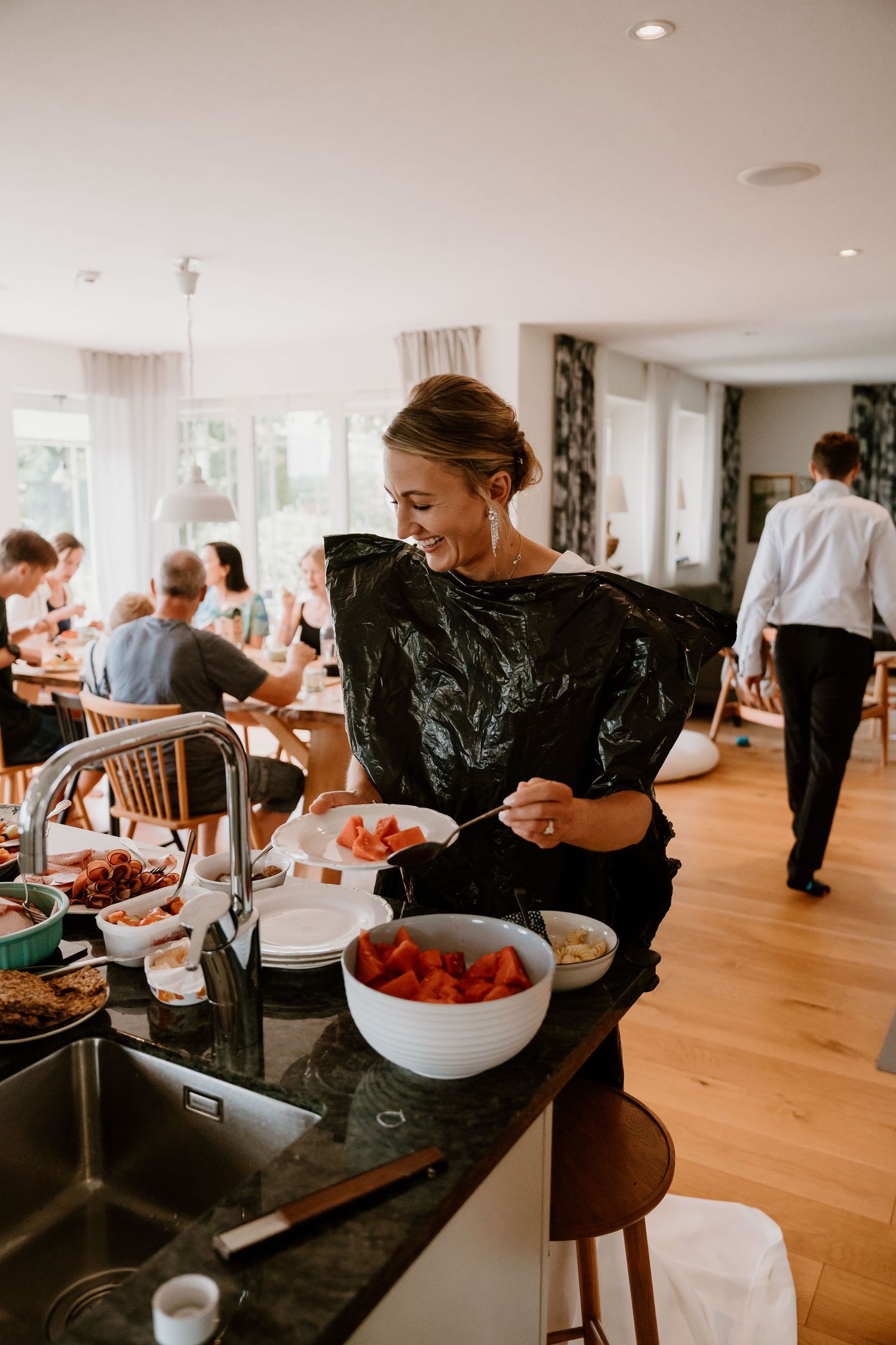 People gather at a buffet style catering setup in a bright modern dining room with hardwood floors and white walls.