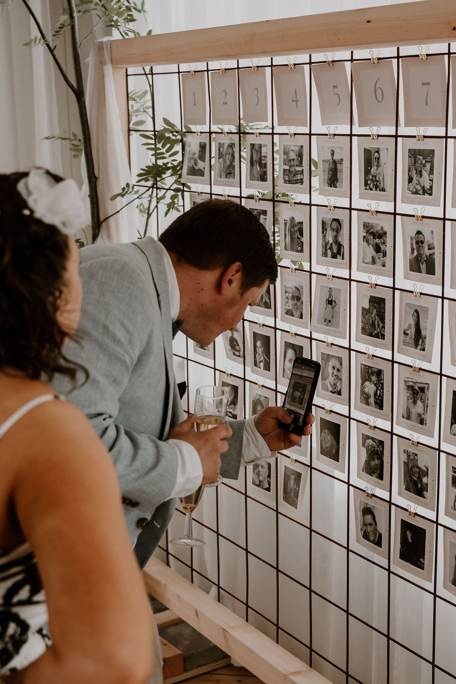 Visitors examine a wall gallery of black and white photographs displayed in a white-walled exhibition space.