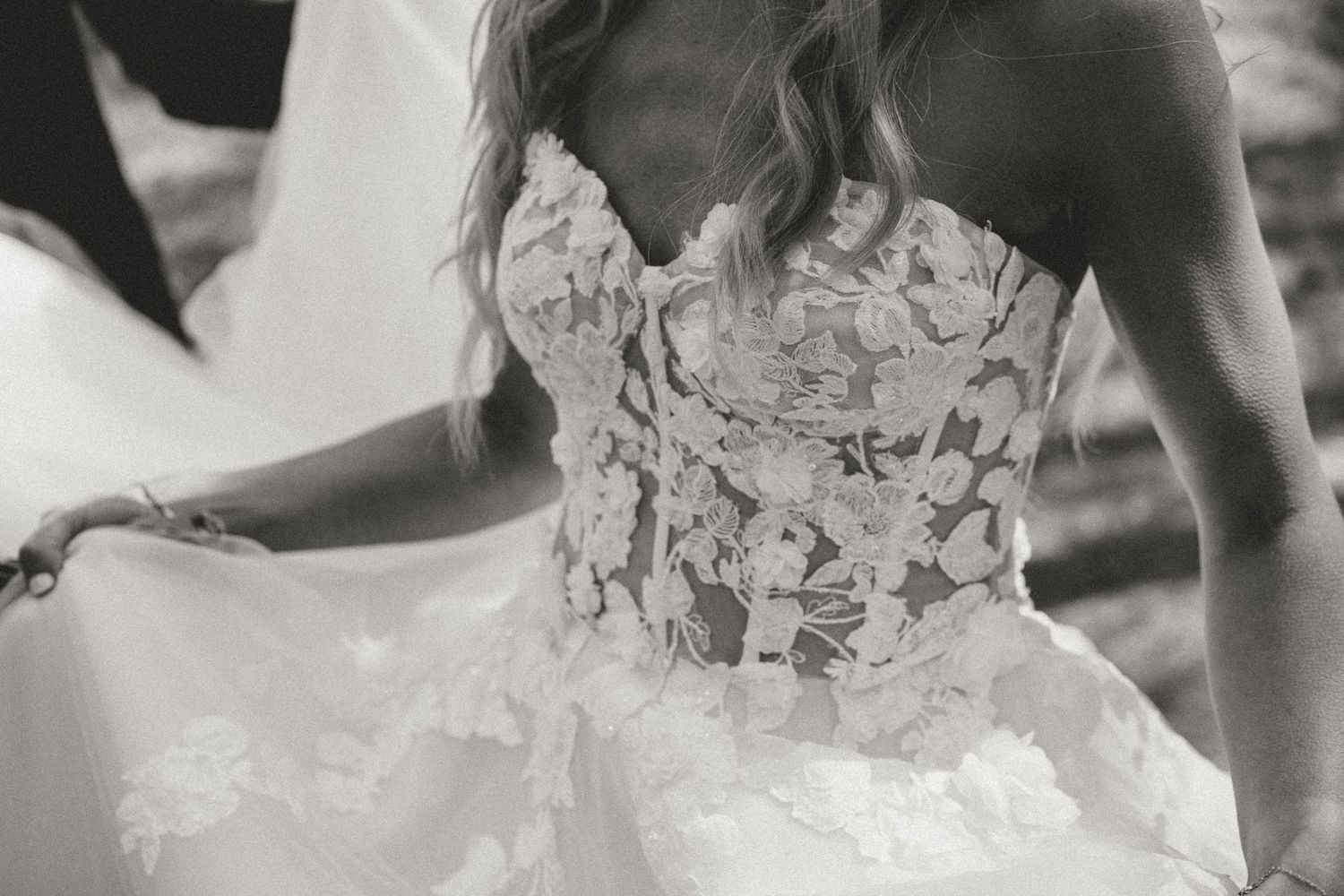 Black and white close-up detail of a wedding dress bodice with intricate floral lace appliques and tulle skirt.