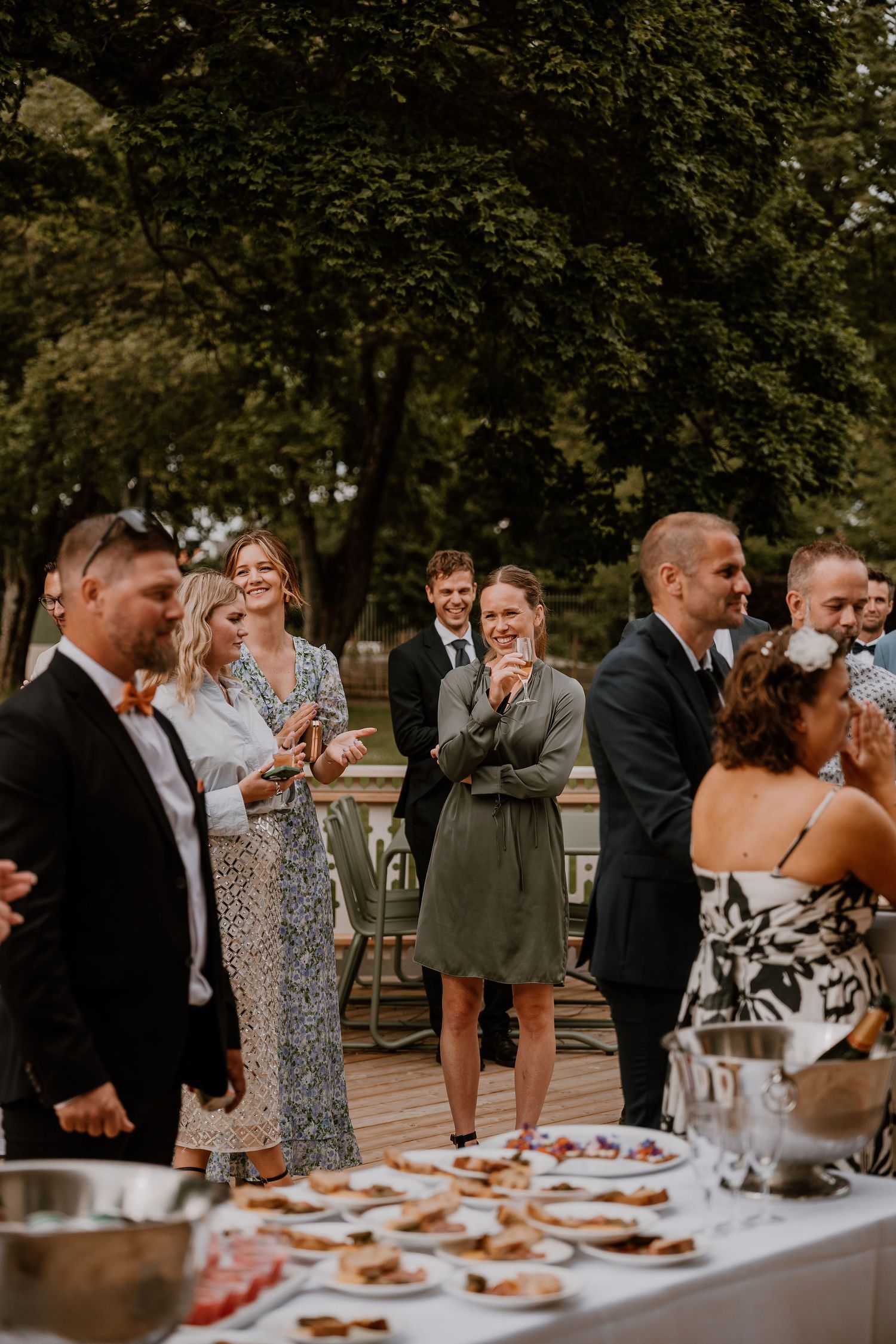 Wedding guests socialize and gather around a buffet table during an outdoor reception celebration.