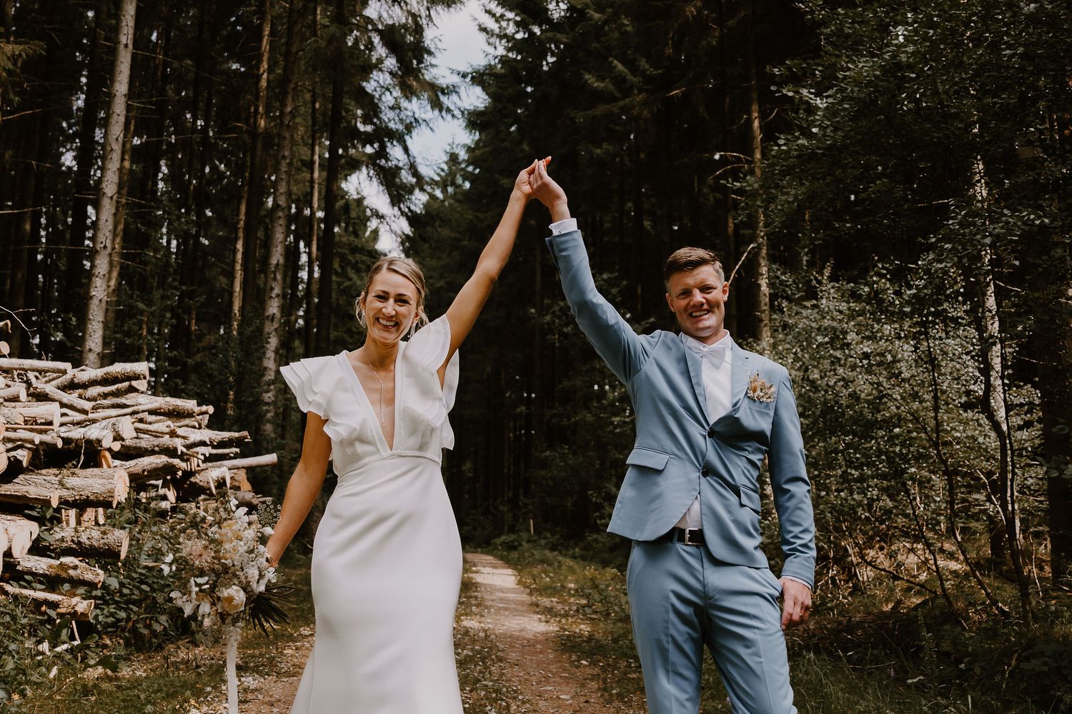 A couple dances joyfully together in a wooded forest setting during their intimate outdoor wedding ceremony.