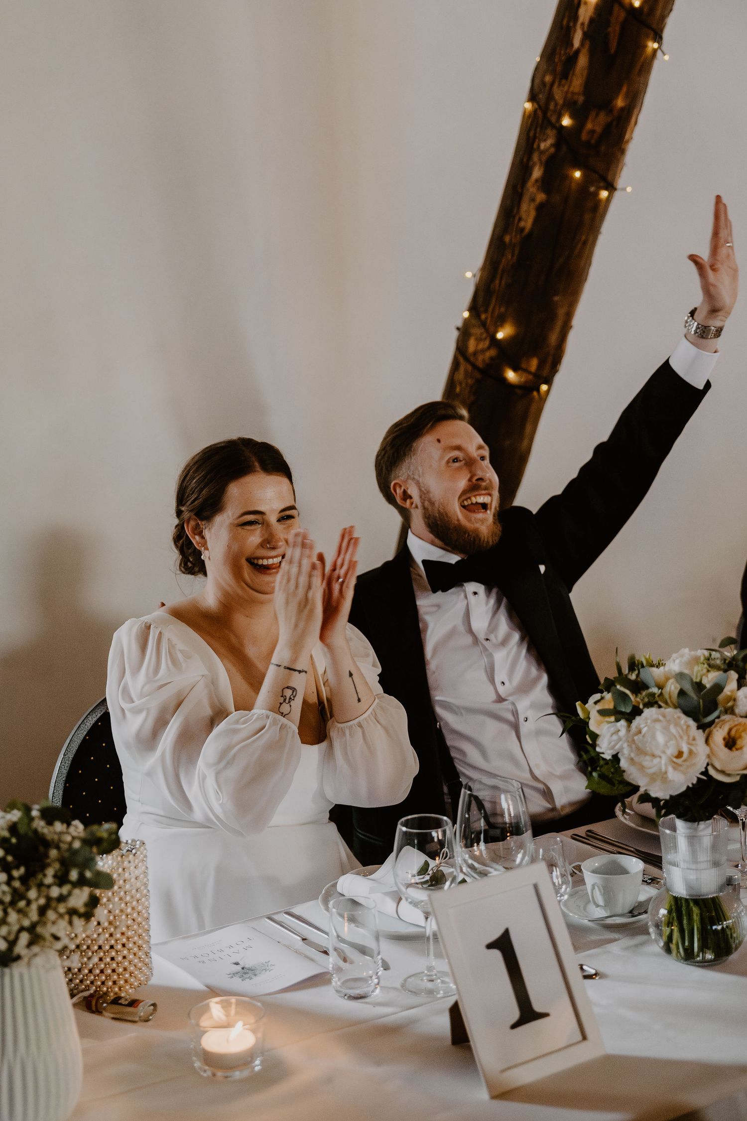 Newlyweds share a joyous moment of laughter at their wedding reception table decorated with floral centerpieces.