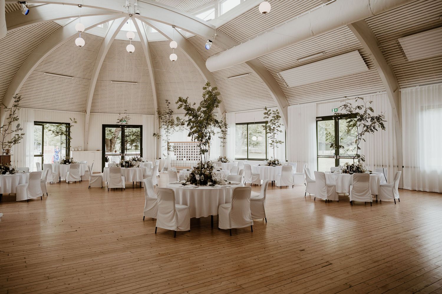 Elegant white wedding reception venue with vaulted ceiling, round dining tables, and natural light streaming through skylights.