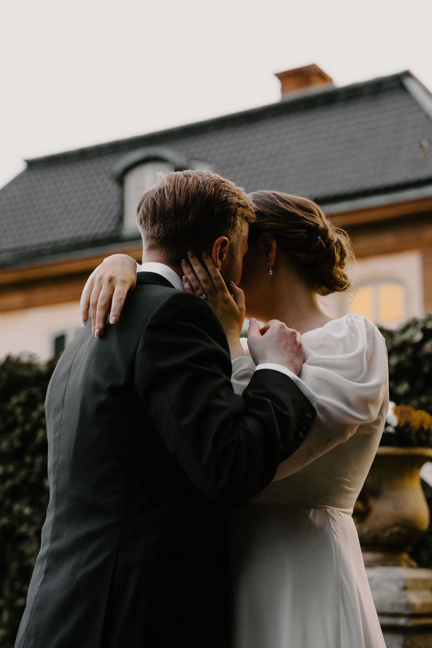 A wedding couple embraces in silhouette against a moody sky during sunset at their outdoor ceremony.