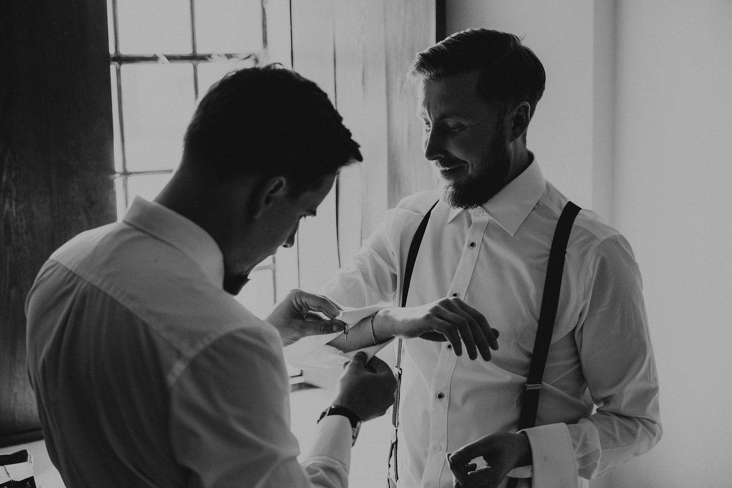 Wedding party members assist with formal preparations in black and white candid shots showing morning attire adjustments.