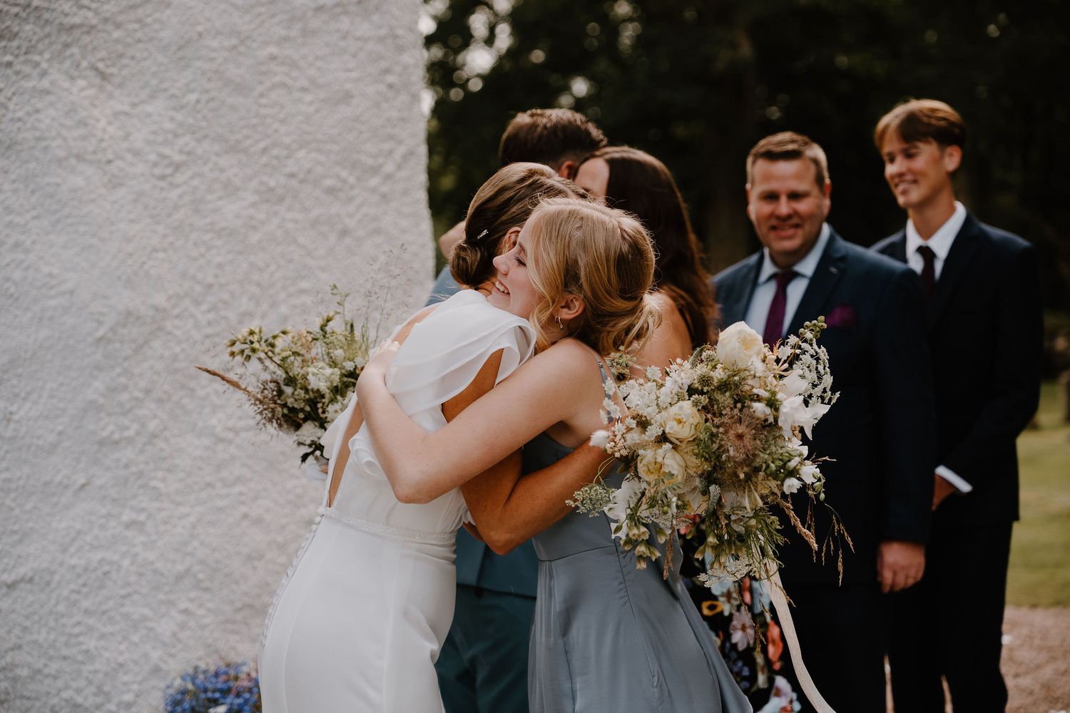 Candid photos from a wedding celebration showing emotional embraces and tender moments between guests outdoors.