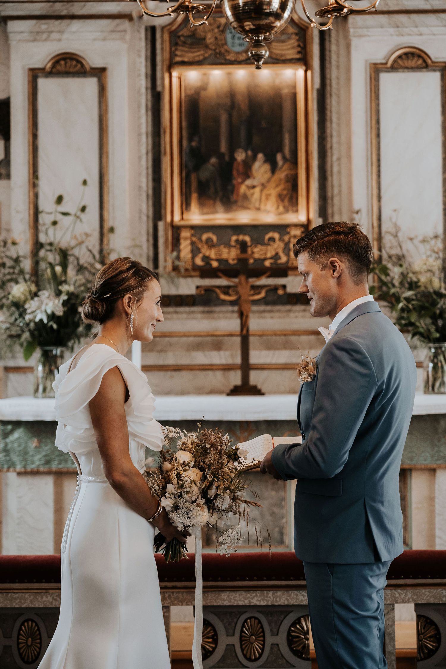 A couple exchanges emotional vows during an intimate church wedding ceremony with ornate decor and floral arrangements.