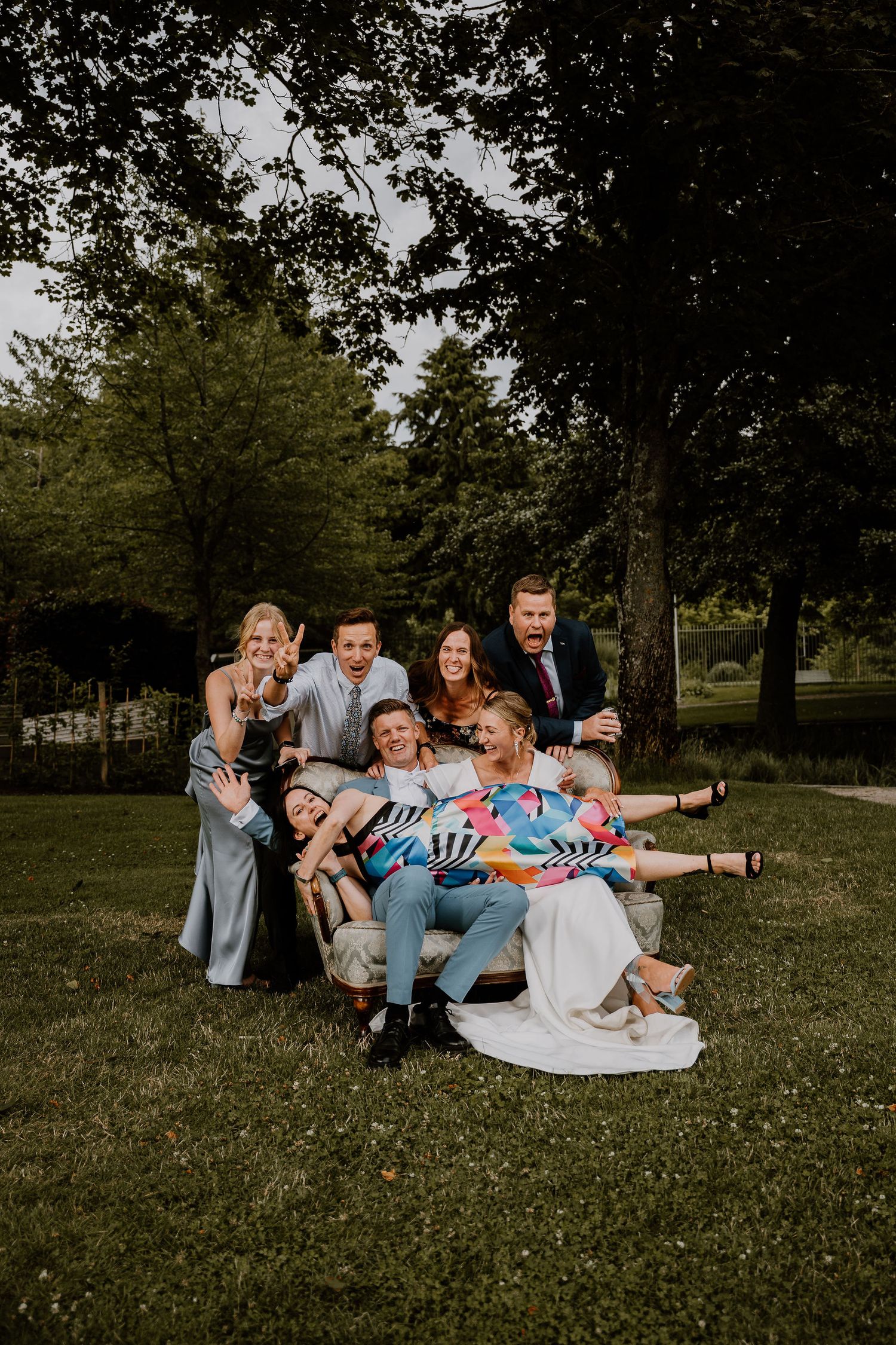 A group of people sit together on wooden benches outdoors in a park setting at dusk.