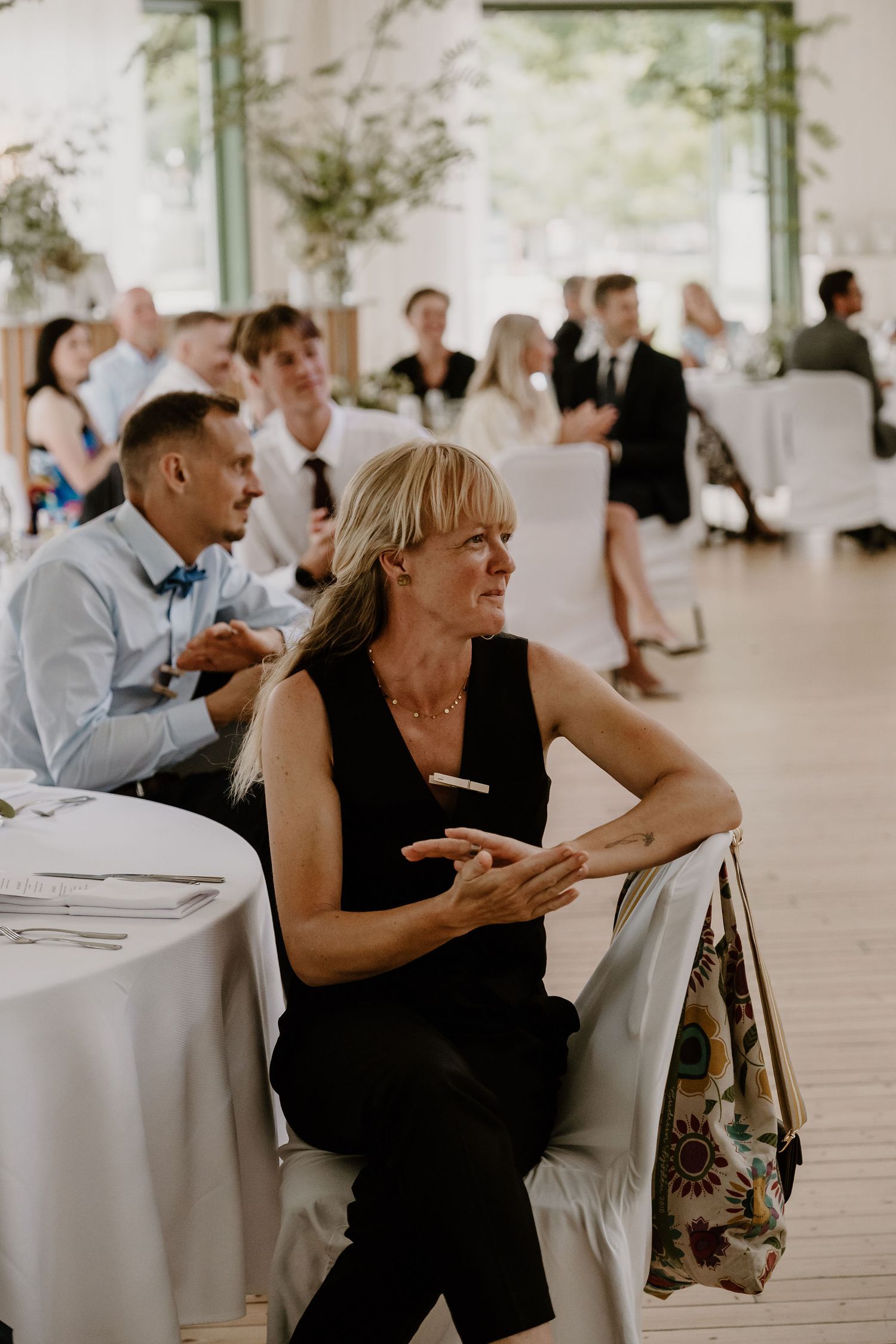 Four candid reception moments show guests enjoying an elegant dining space with white tablecloths in a light-filled venue.