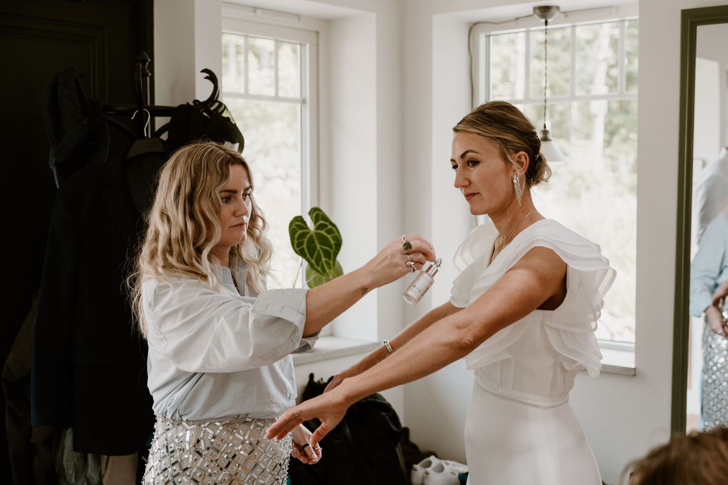 Two people in white garments helping each other get dressed in a bright sunlit room.
