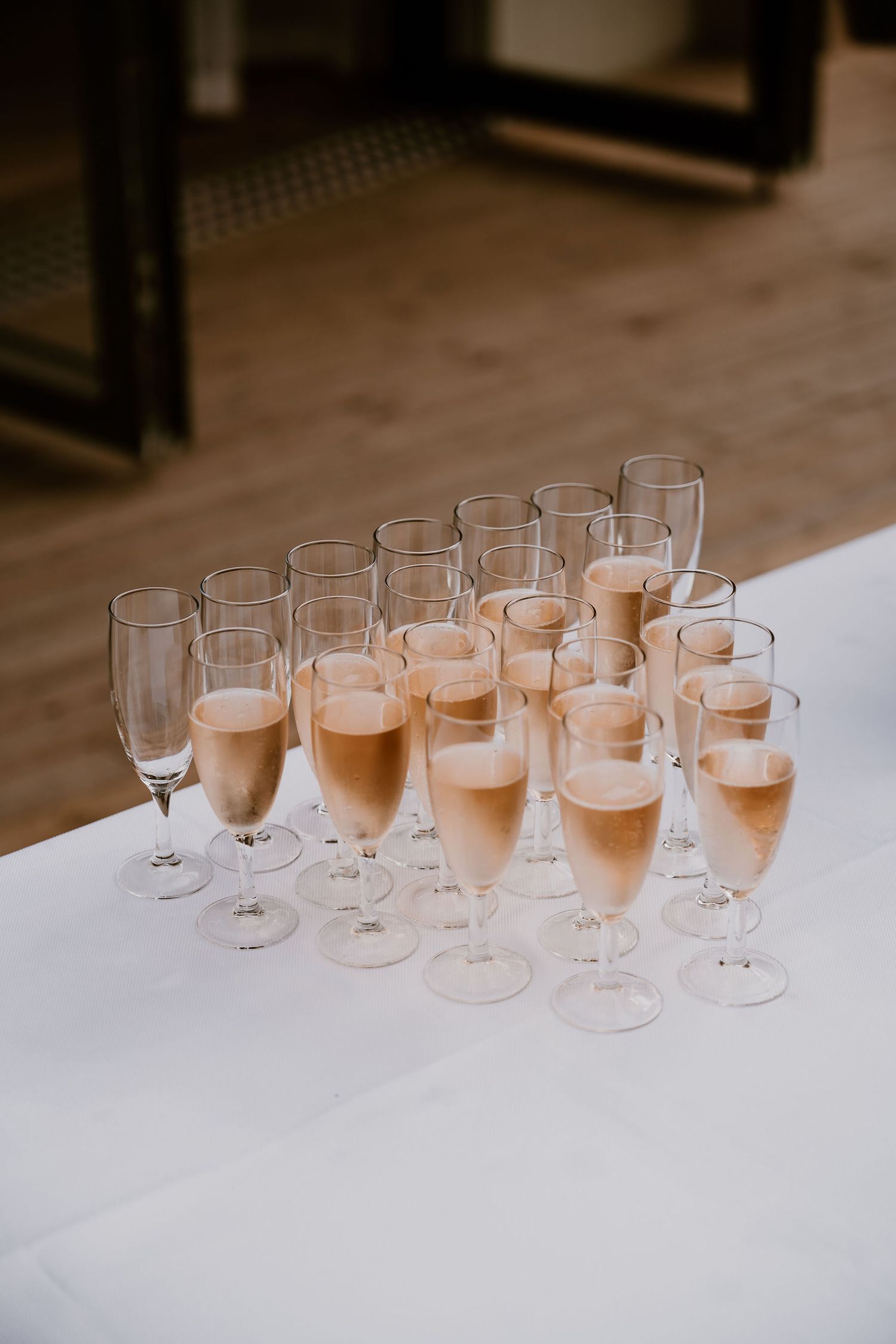 Multiple champagne flutes filled with rose-colored sparkling wine arranged in neat rows on a white surface.