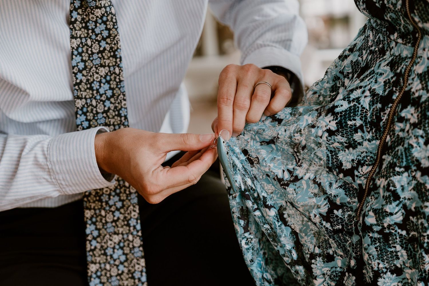 Close up shot of hands touching delicate teal floral lace fabric next to a floral print tie.