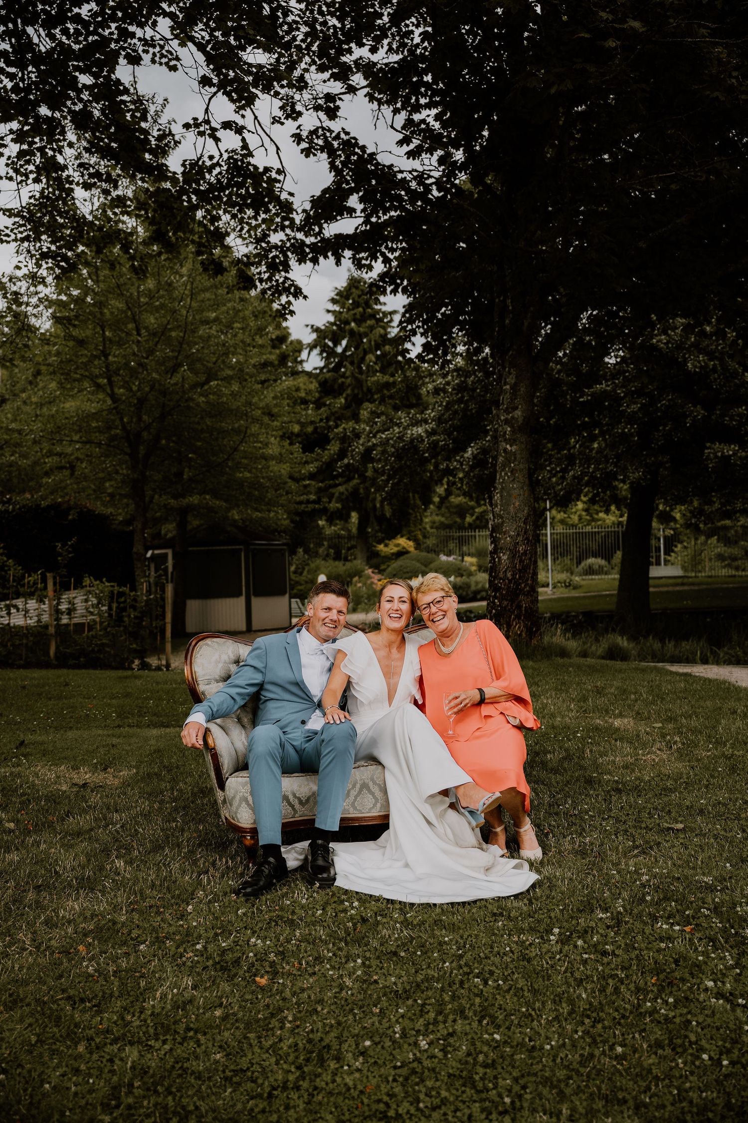 A group sits together outdoors on a vintage couch in a park setting during golden hour.