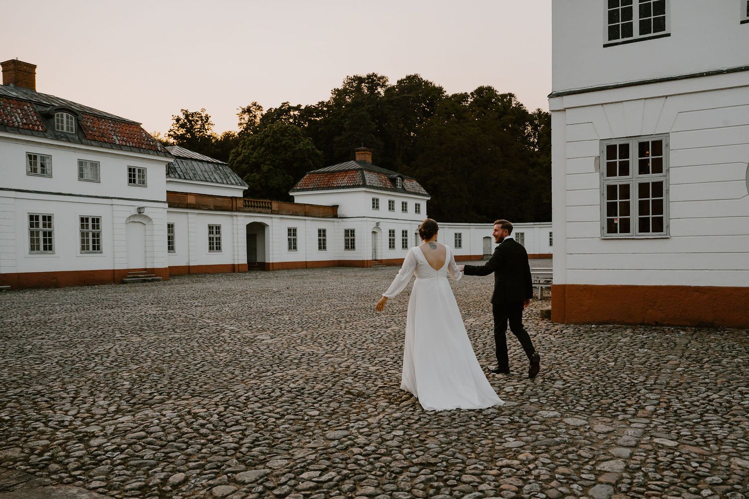Couple dances together on historic cobblestone courtyard surrounded by elegant white buildings at sunset.