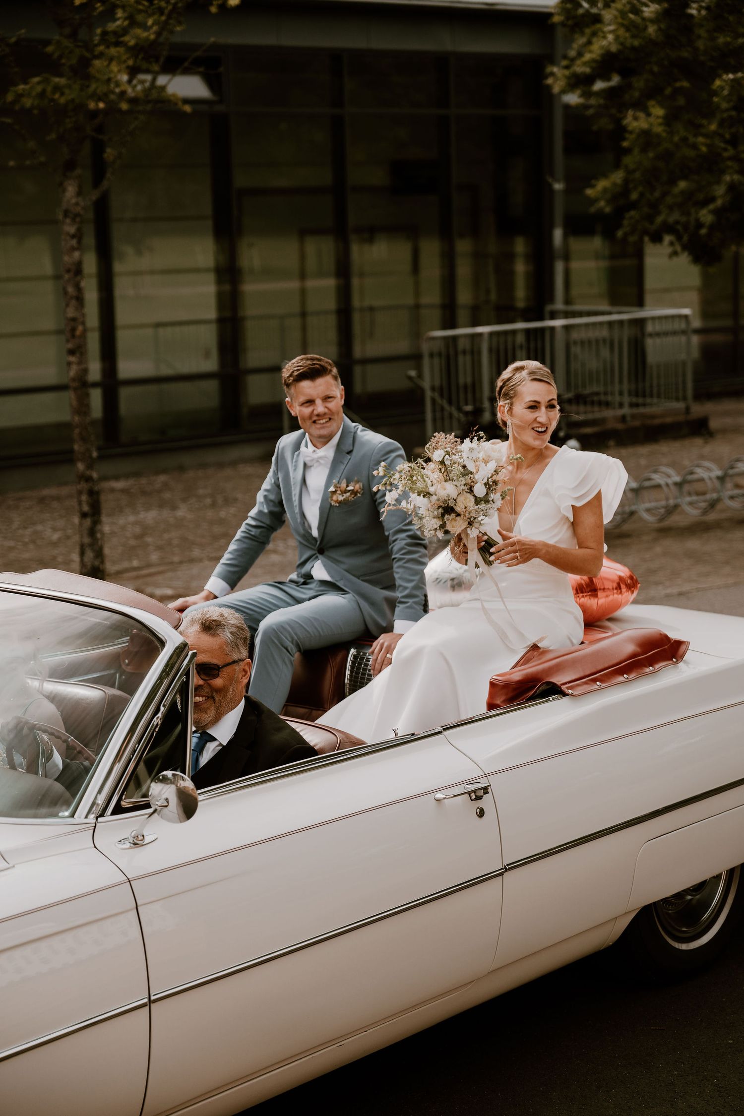 Newlywed couple sitting in a vintage white convertible car during their wedding celebration.