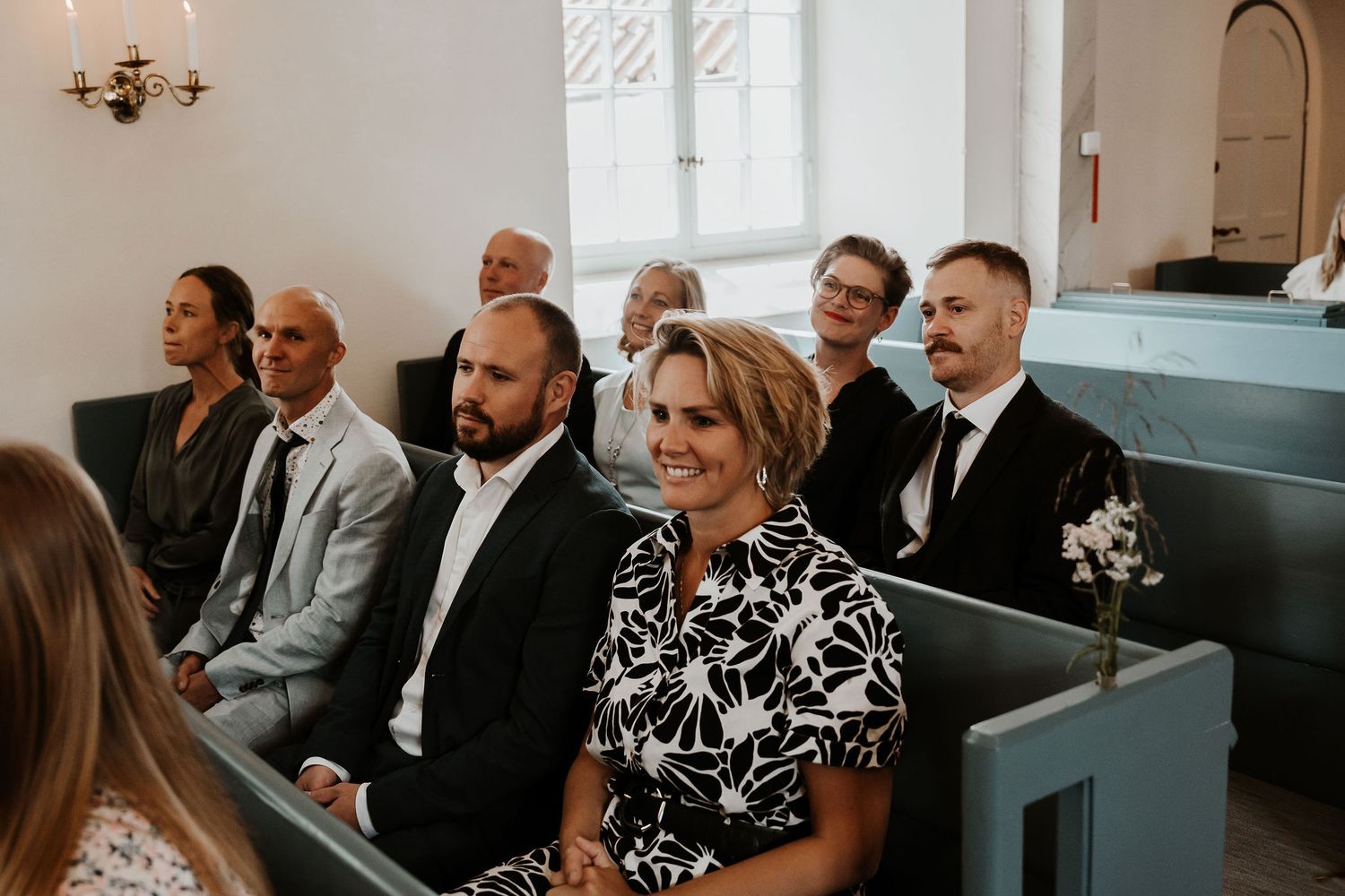 Wedding guests sit in wooden church pews watching an emotional ceremony with light streaming through the windows.