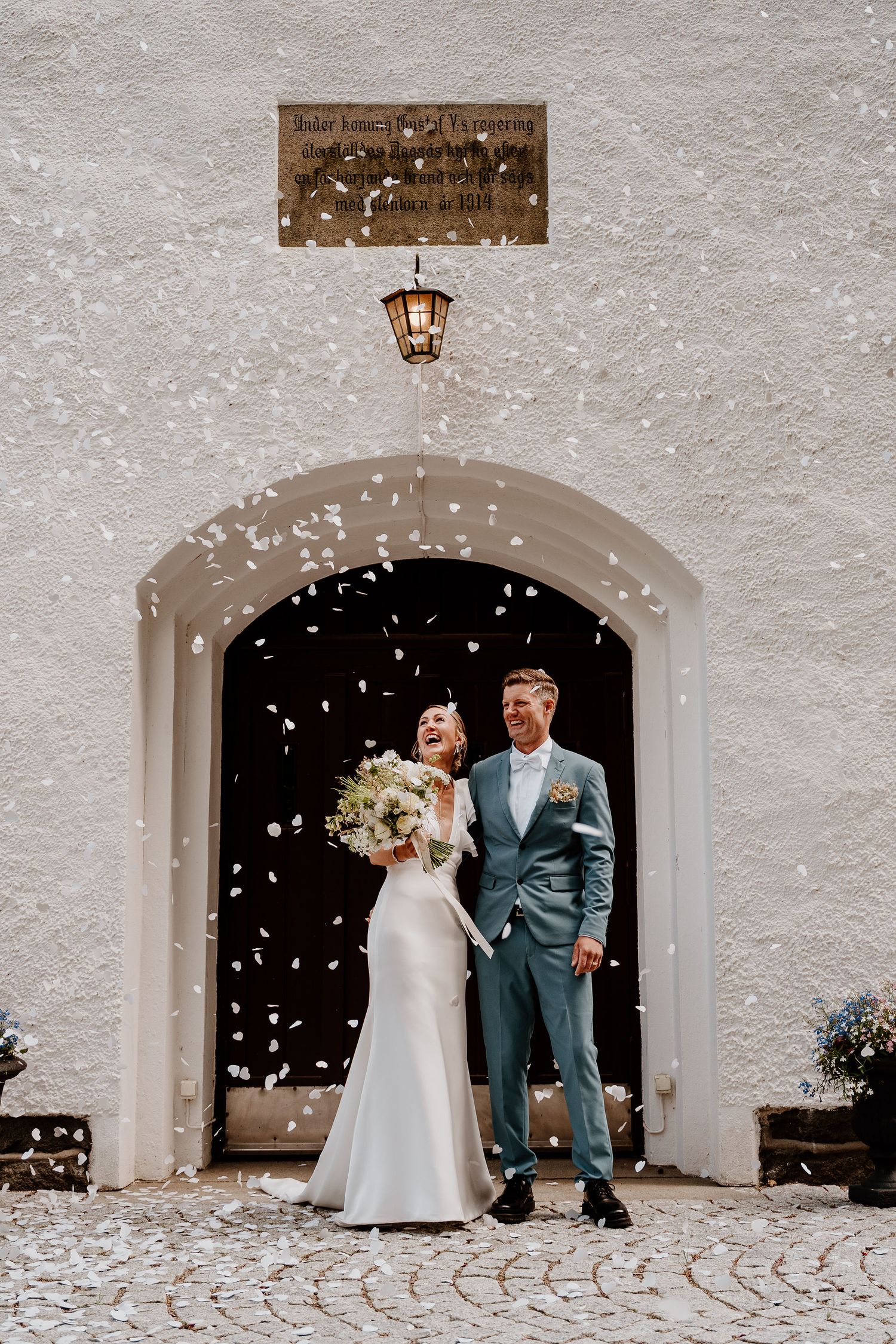 White confetti falls around an elegant arched doorway with lantern as a couple celebrates at their outdoor wedding ceremony.