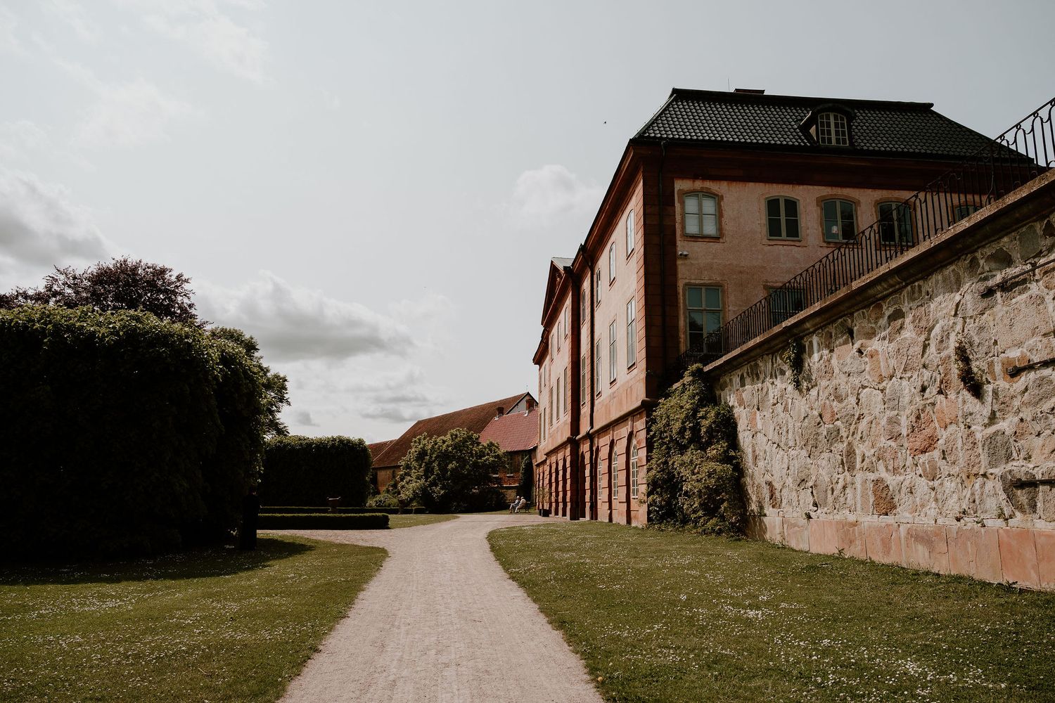 A winding path leads past an old stone wall and brick building under cloudy skies at a historic fortress.