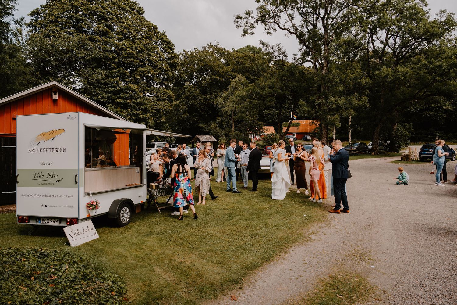 Outdoor event space with multiple small orange buildings and gravel paths surrounded by green trees.