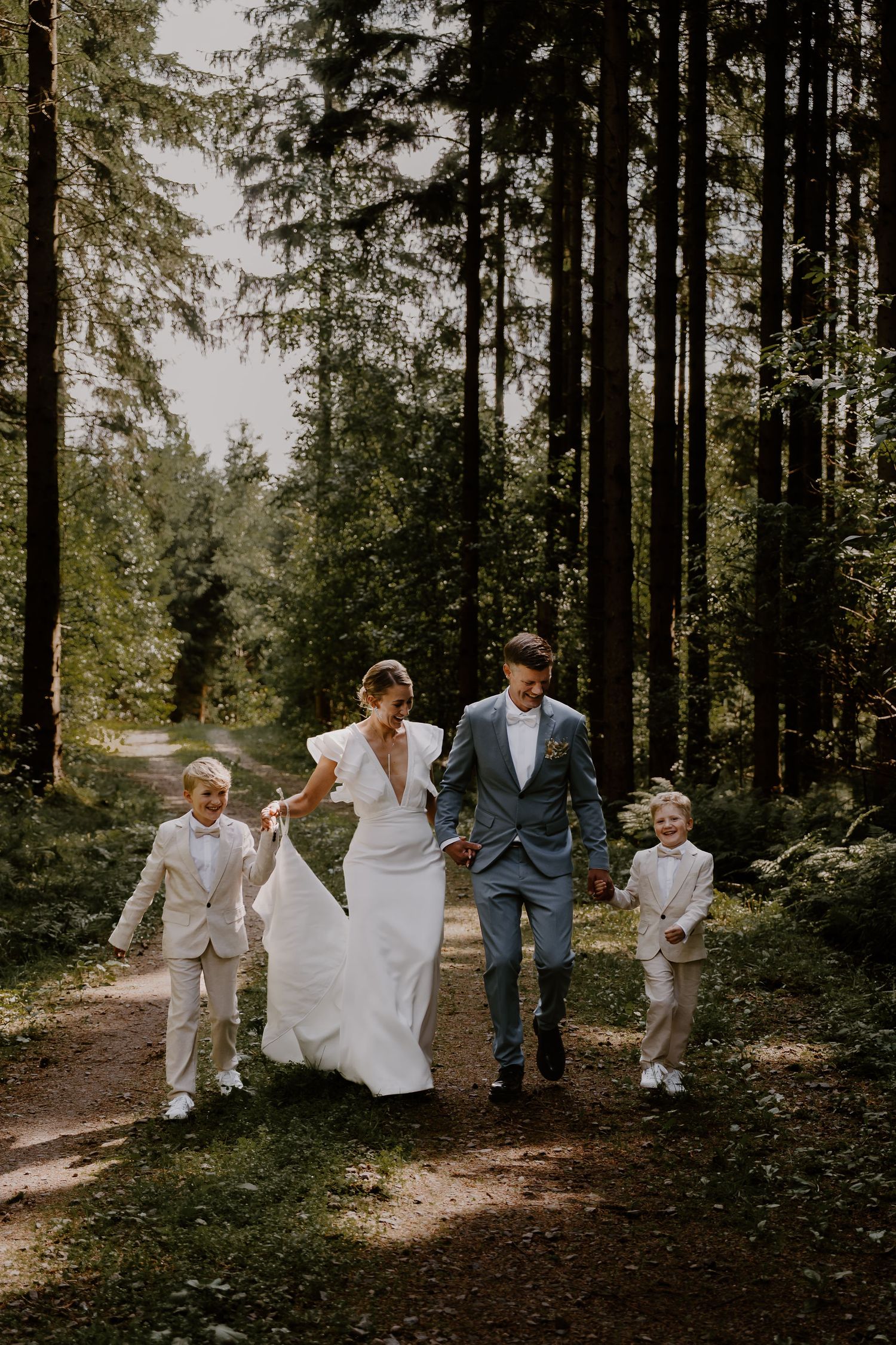 Wedding party joyfully walks through a forest path with evergreen trees in the background.