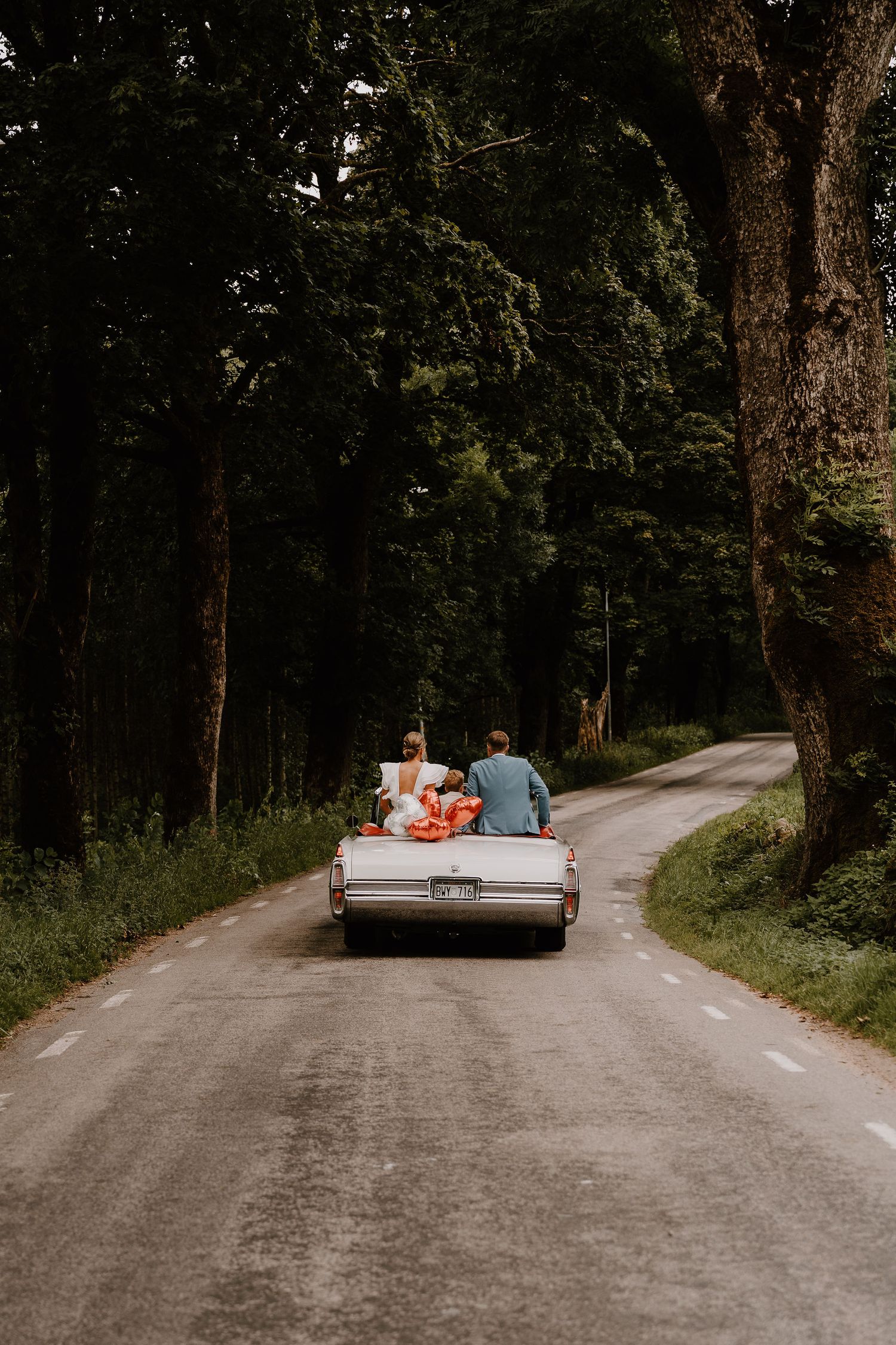 A couple sits on a cream-colored couch in an outdoor wooded setting, creating an artistic photo series on a dirt path.