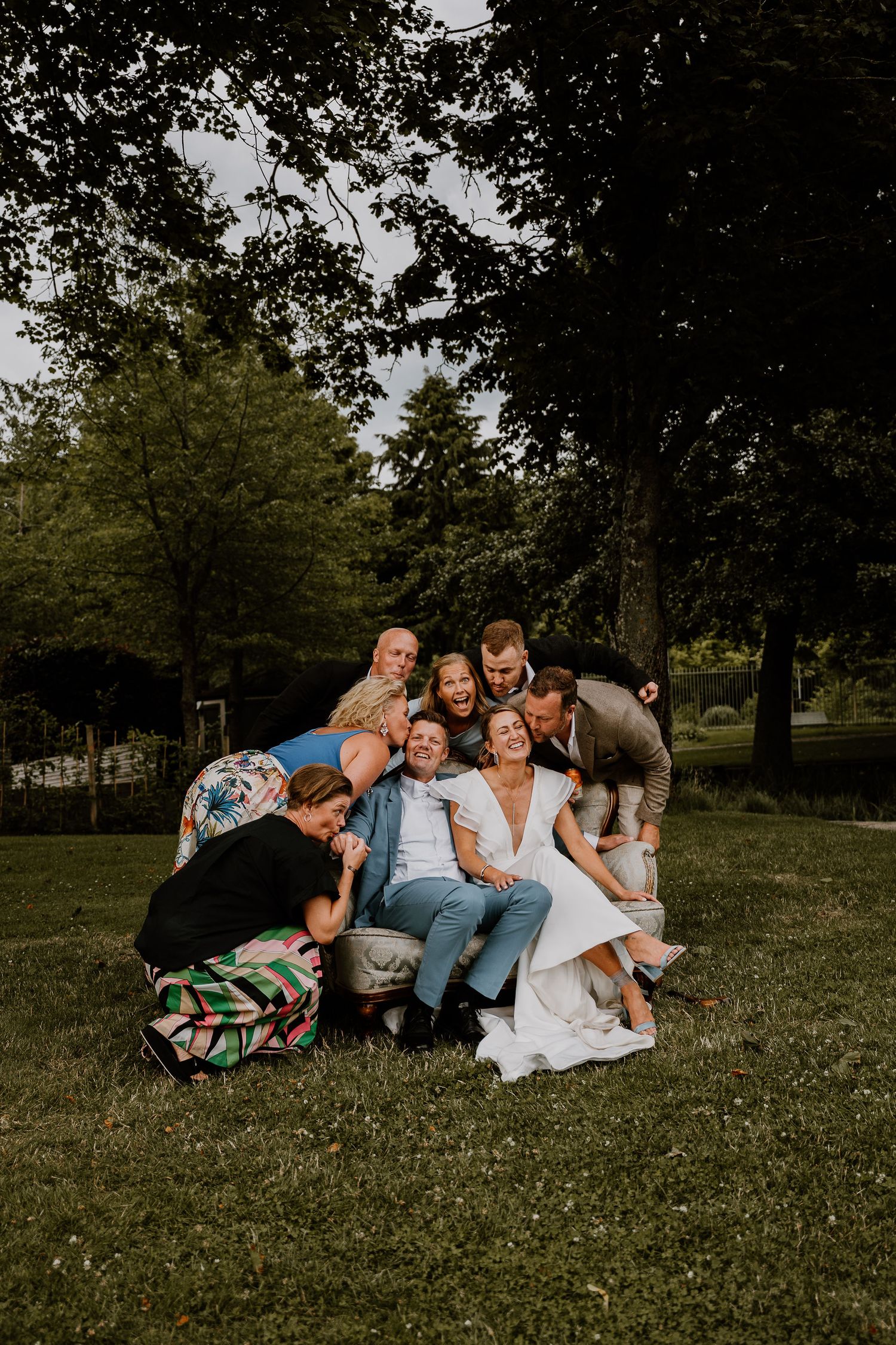 A group of friends lying together on grass in a park under trees during a casual outdoor gathering.