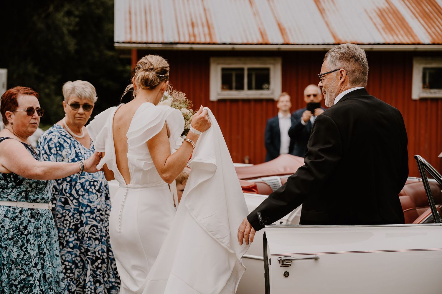 A group of people celebrating outside a rustic red barn building during what appears to be a wedding celebration.