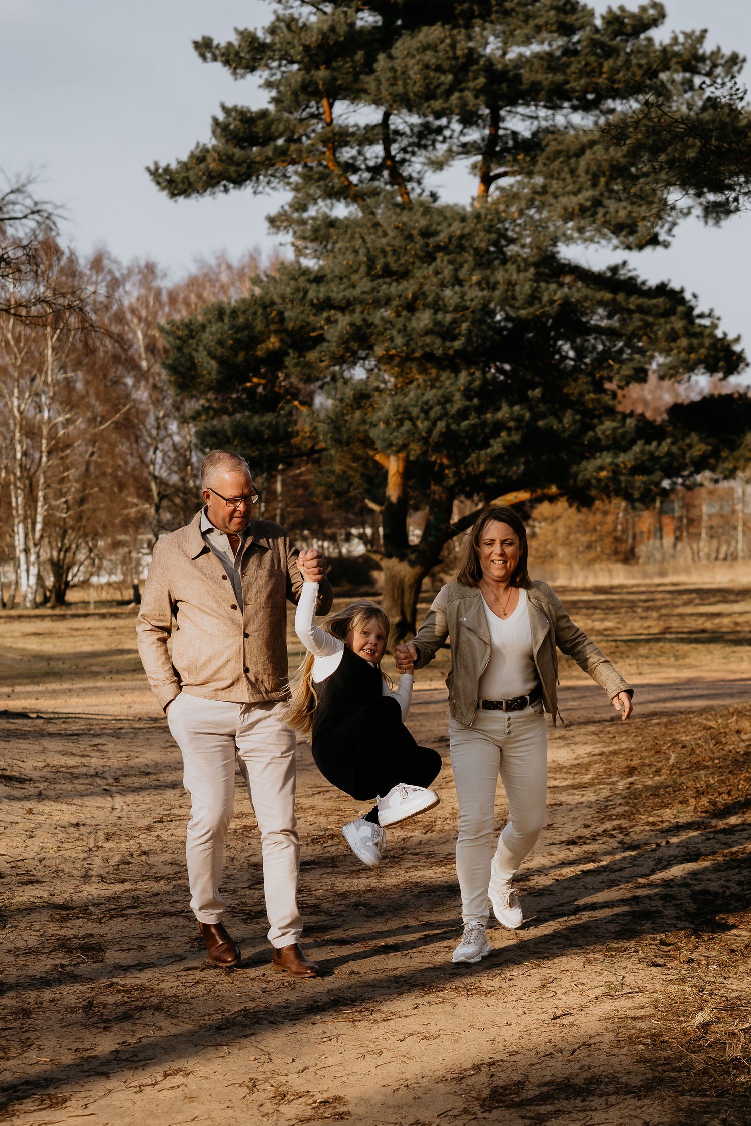 Happy family enjoying a playful walk together in a natural setting with pine trees on a sunny autumn day.
