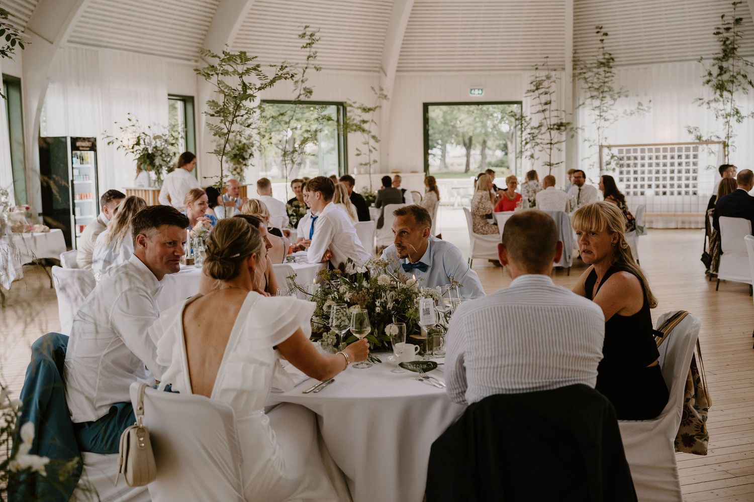 Elegant wedding reception setup with draped white fabric ceiling and greenery decorations in a bright airy venue.