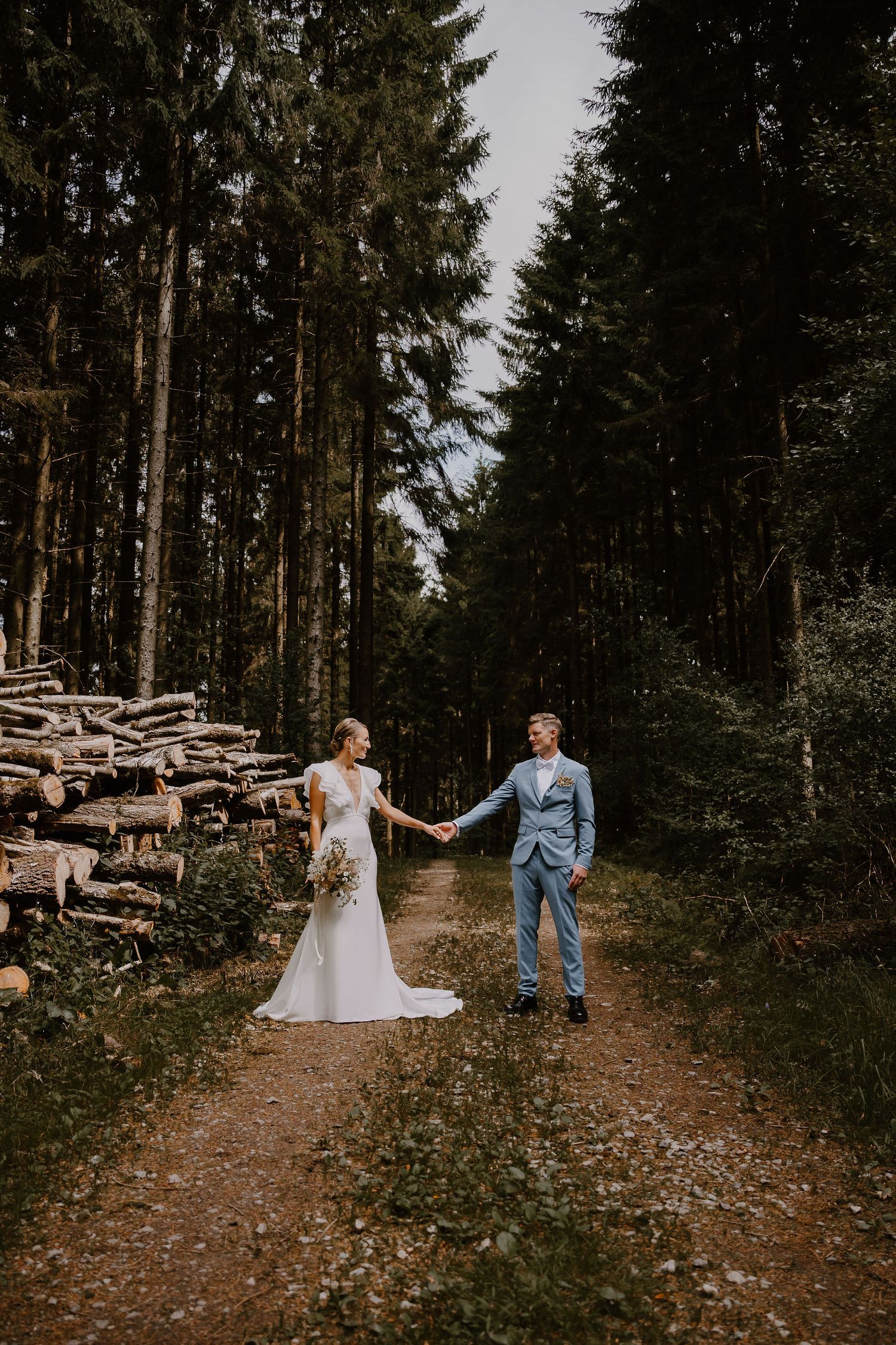 A romantic forest wedding photoshoot sequence showing a couple posing near stacked logs on a dirt path.
