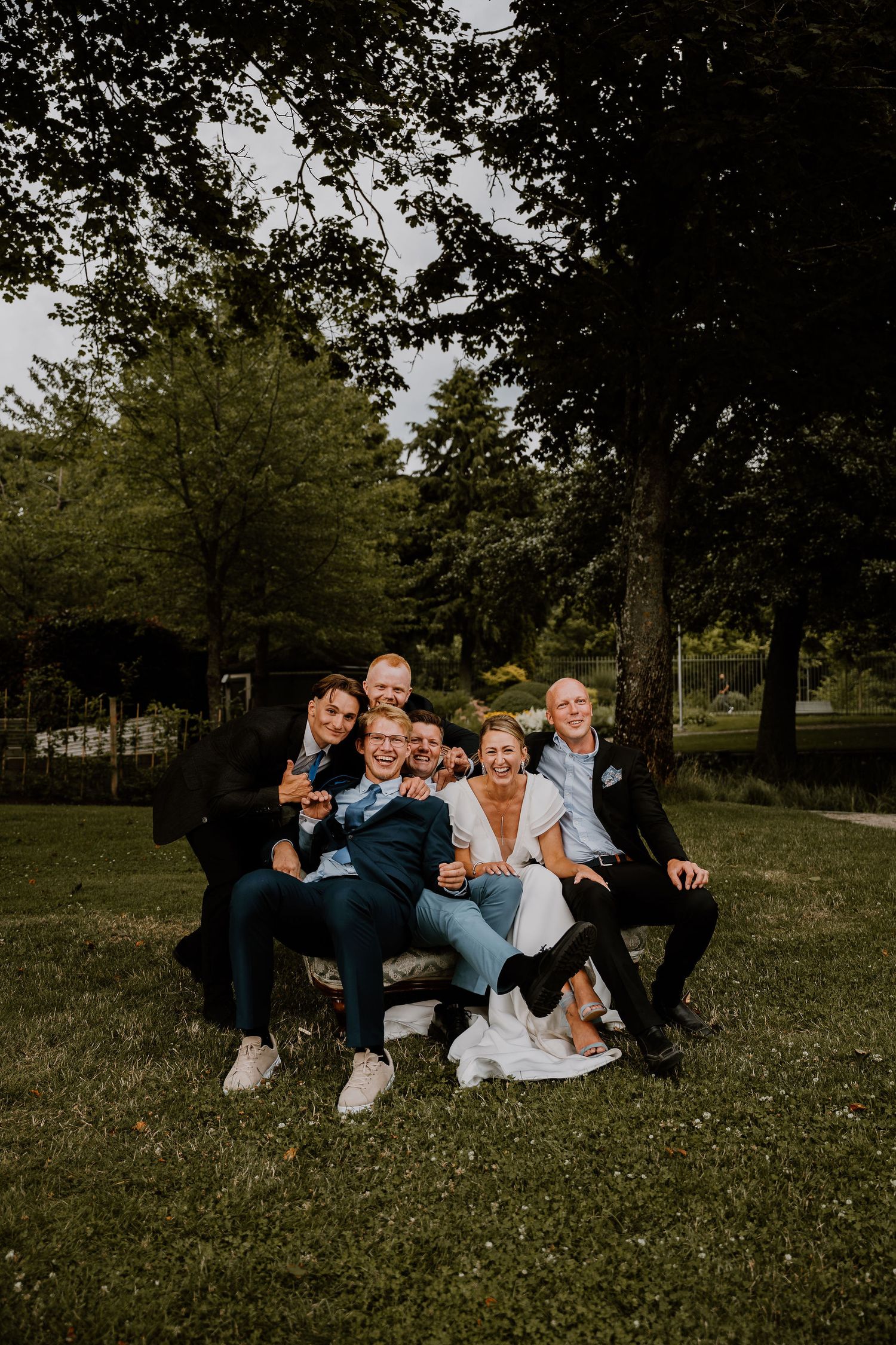 A group relaxes and poses playfully on grass in a park setting during a casual outdoor photo session.