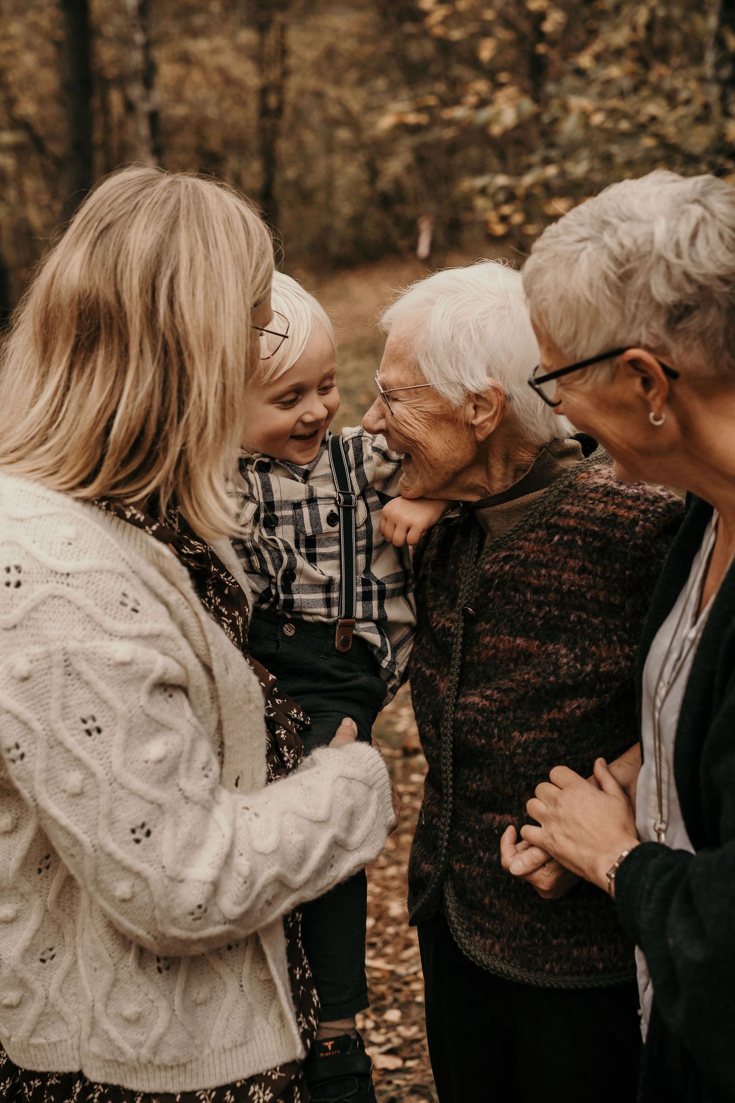 Three generations share a joyful moment of laughter together in an autumn forest setting.