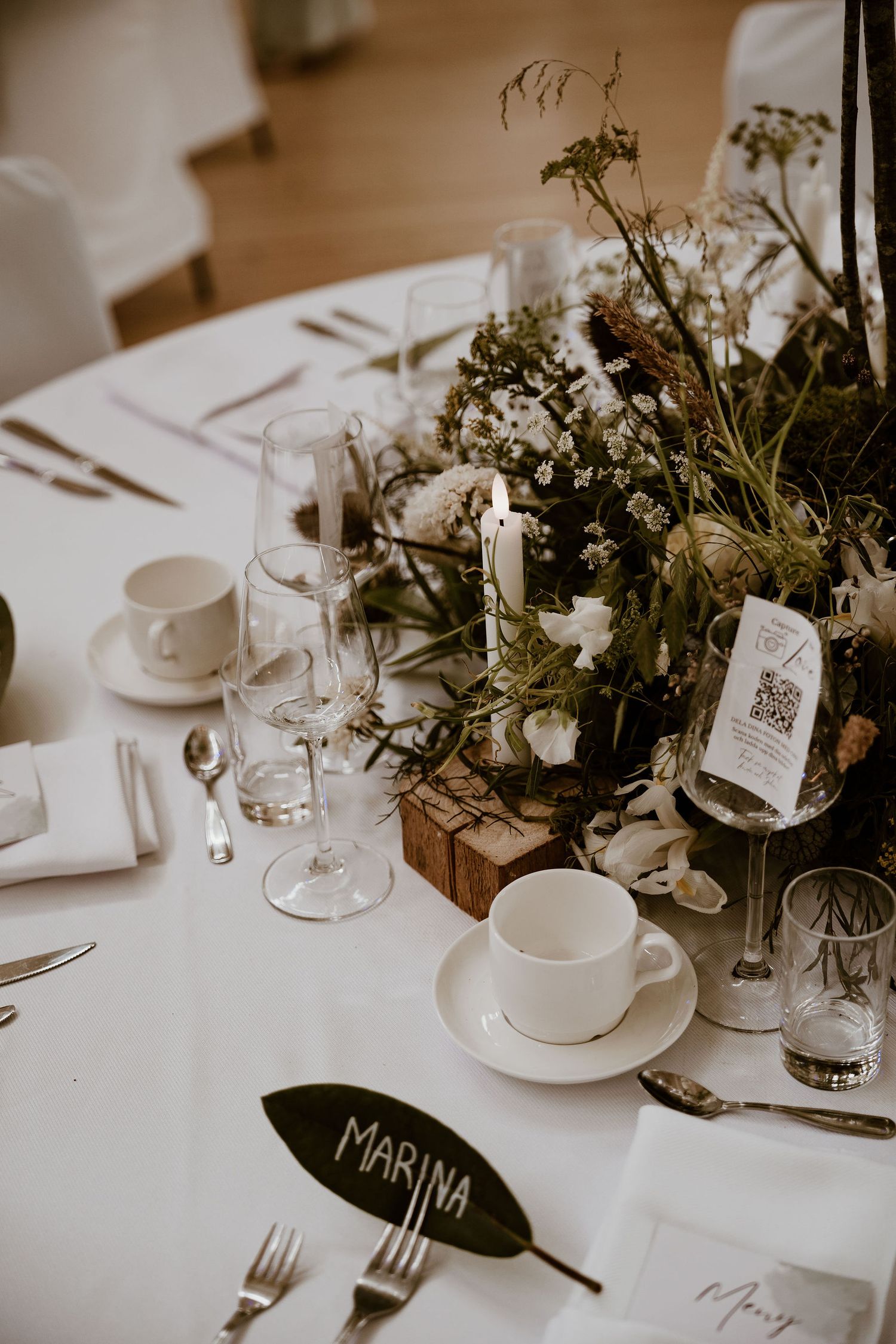 Wedding reception table settings feature elegant floral arrangements and white linens with rustic name cards.