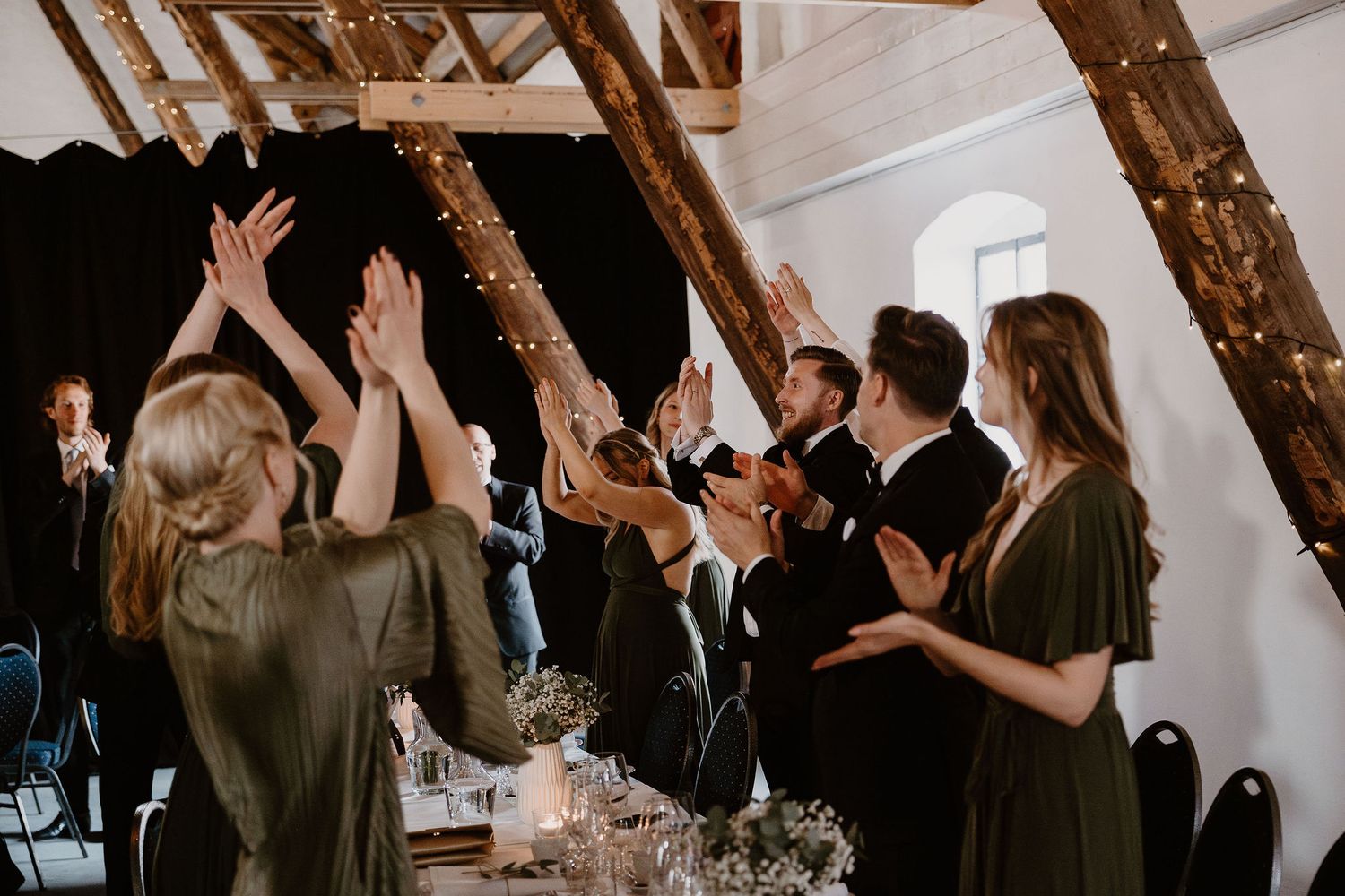 Wedding guests clapping and dancing with hands raised during celebration at a rustic barn reception venue.
