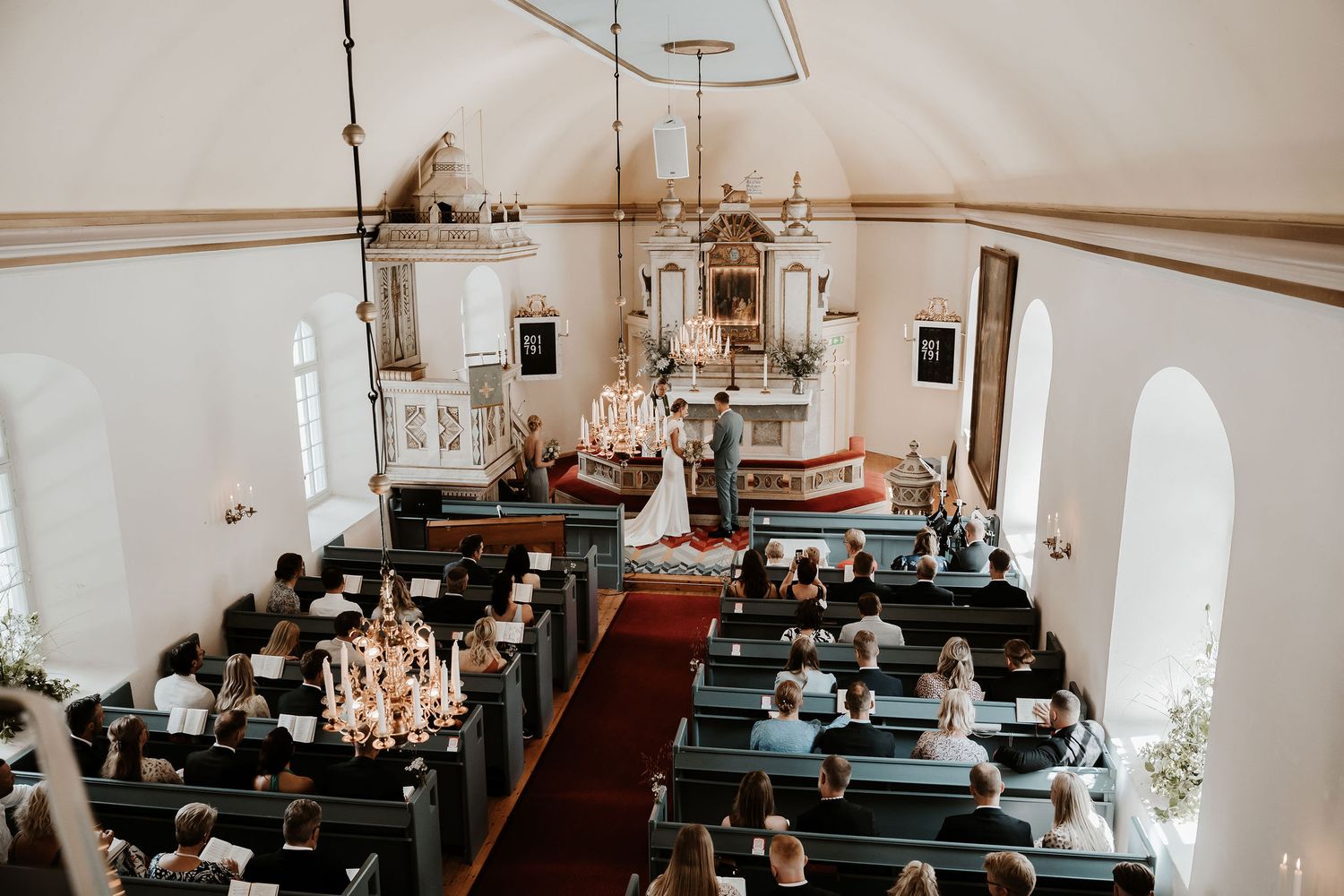 Interior panorama of a rustic church sanctuary with wooden pews and decorative chandeliers.