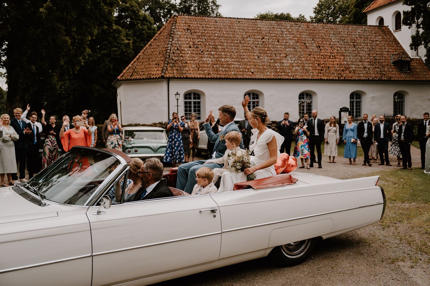 Several white vintage limousines parked in front of a traditional white building during an event.