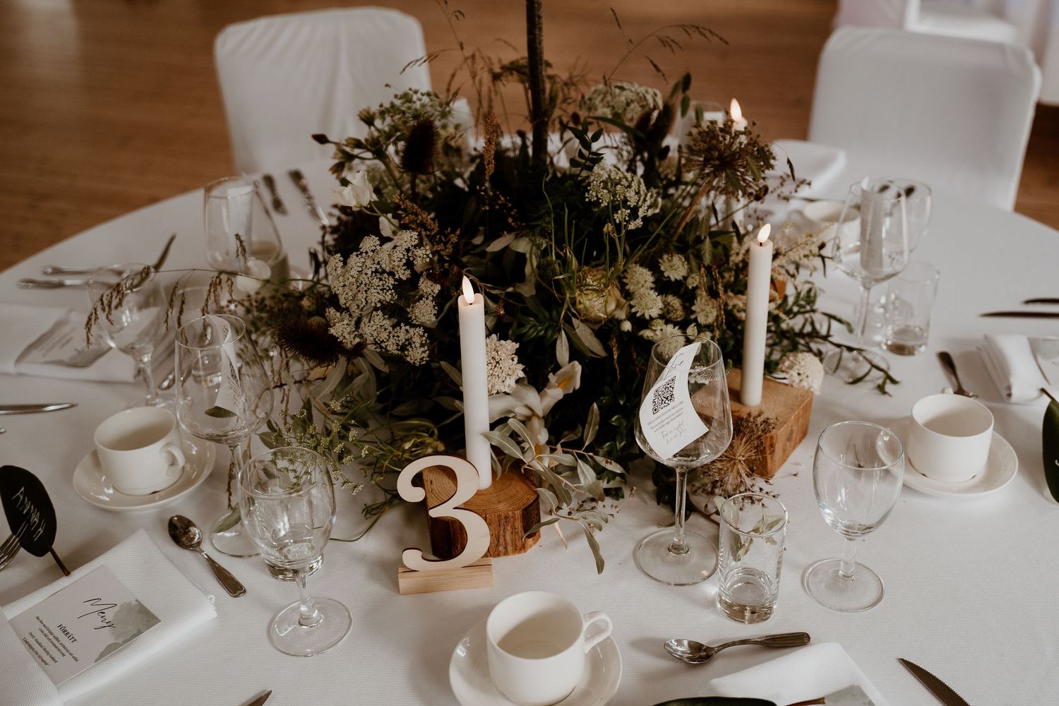 An elegant wedding reception table setting with white linens, crystal glassware and floral centerpiece arrangements.