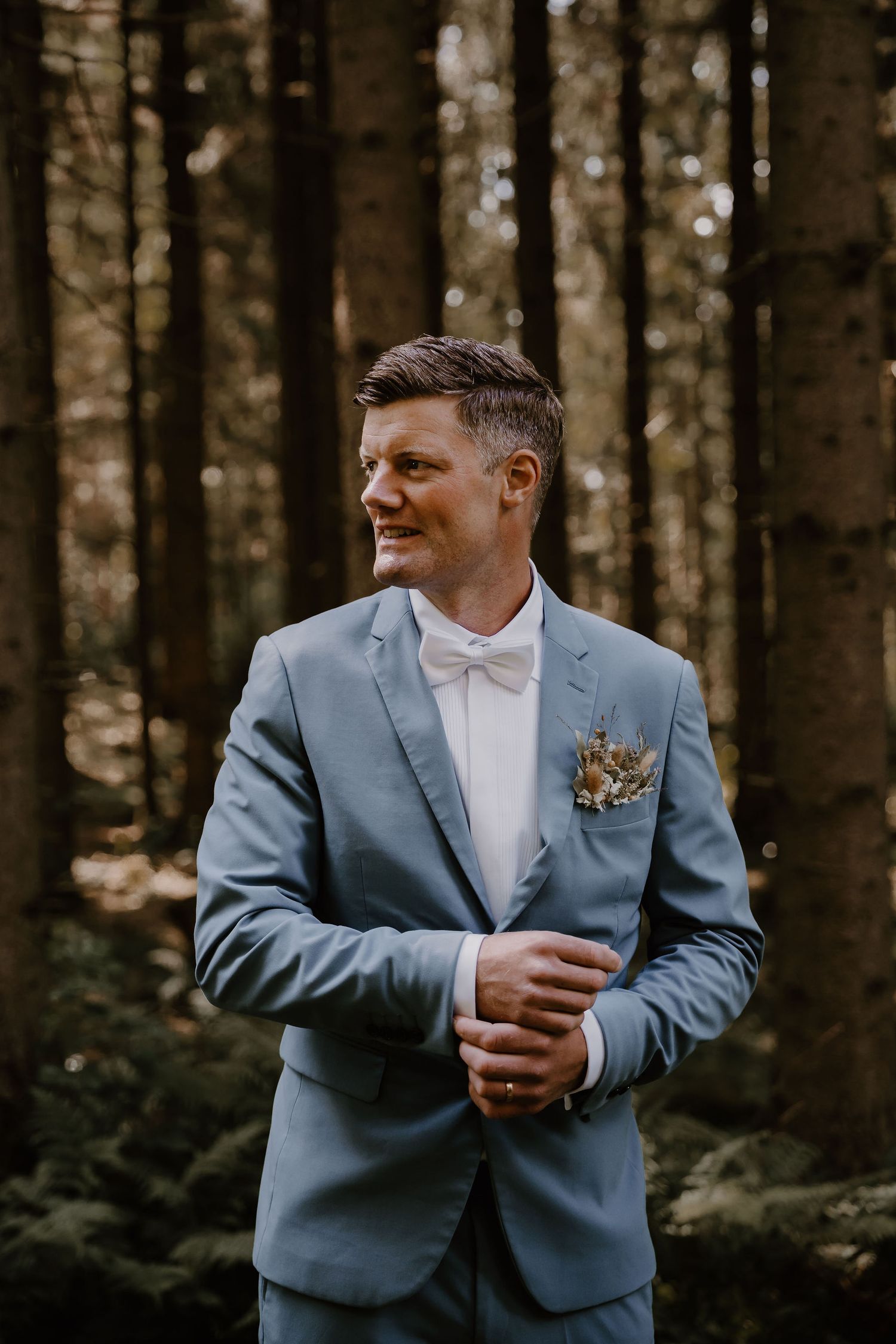 Person in blue suit and white shirt standing in forest with moody lighting and natural background.