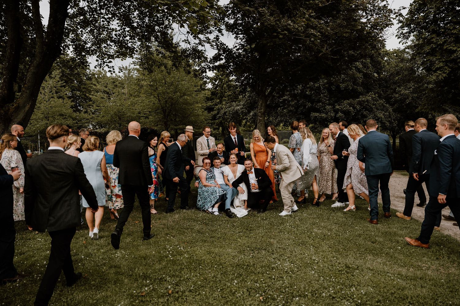Wedding guests gather on a lush green lawn during an outdoor reception celebration on a sunny afternoon.